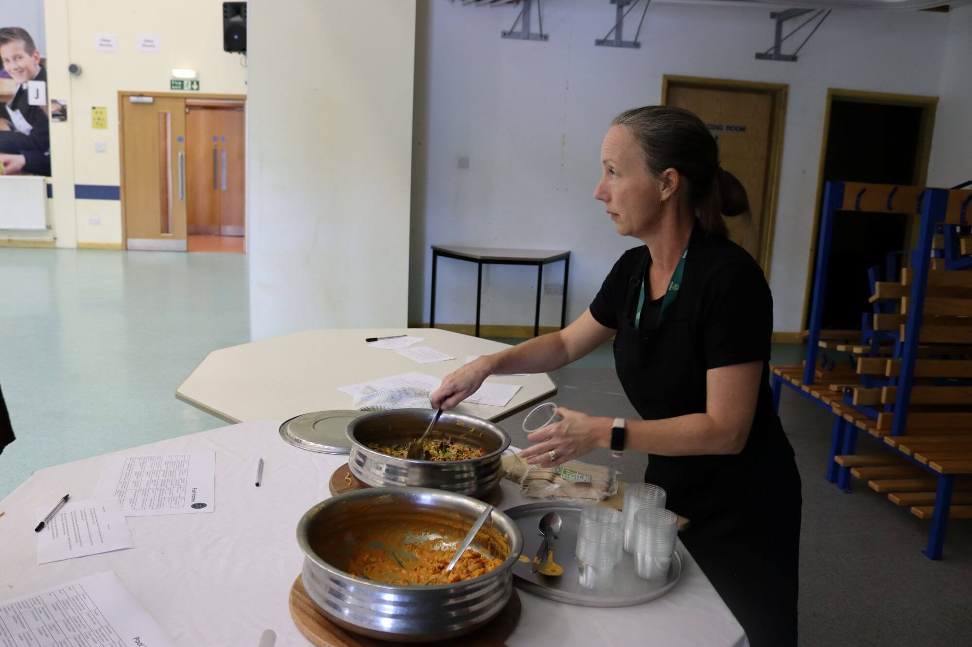 A member of Pool Academy Kitchen staff serving food from steel dishes