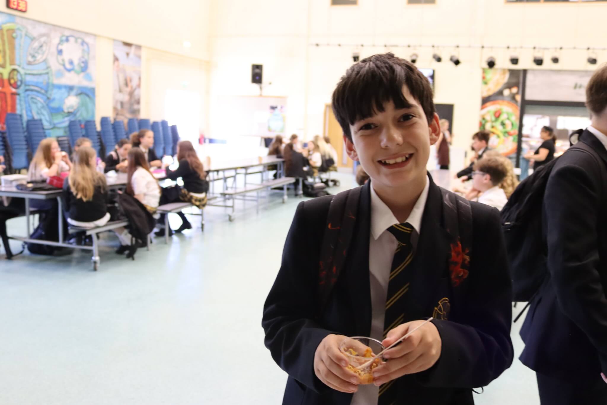 A smiling Pool Academy student holding a pot of food in the school hall