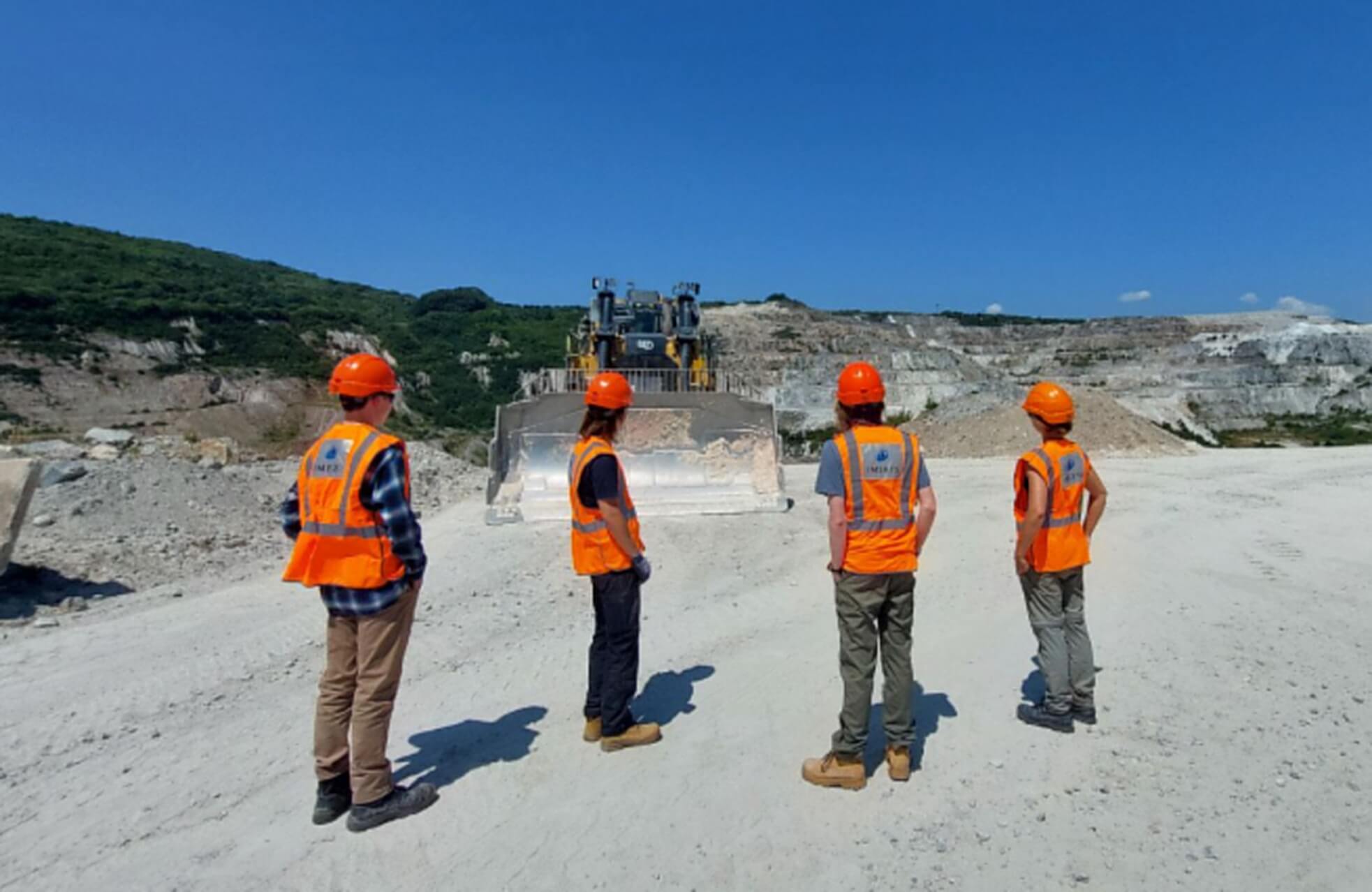 Students in high-vis and hard hats watching a digger at an Imerys quarry in Cornwall