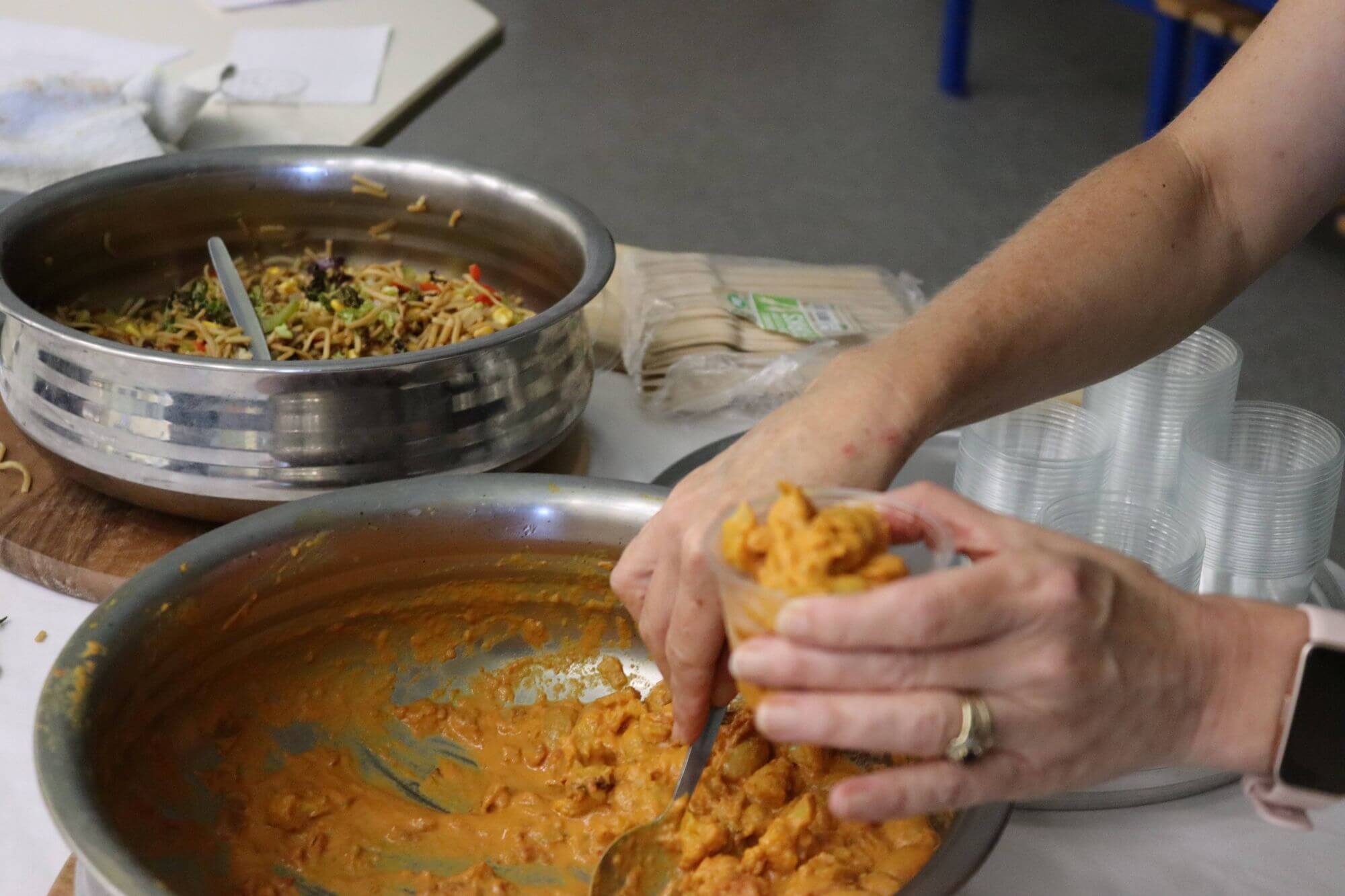 Food being spooned into taster pots from large steel serving dishes