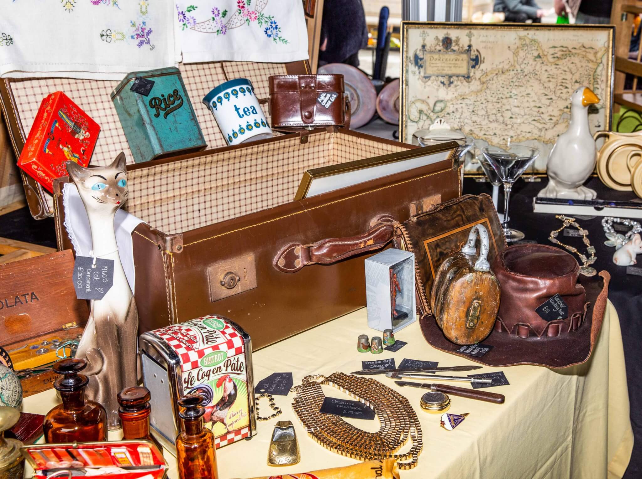 Vintage suitcase, tins, a 1960s cat ornament and collectables on a stall at a previous Truro Antiques and Collectables Market