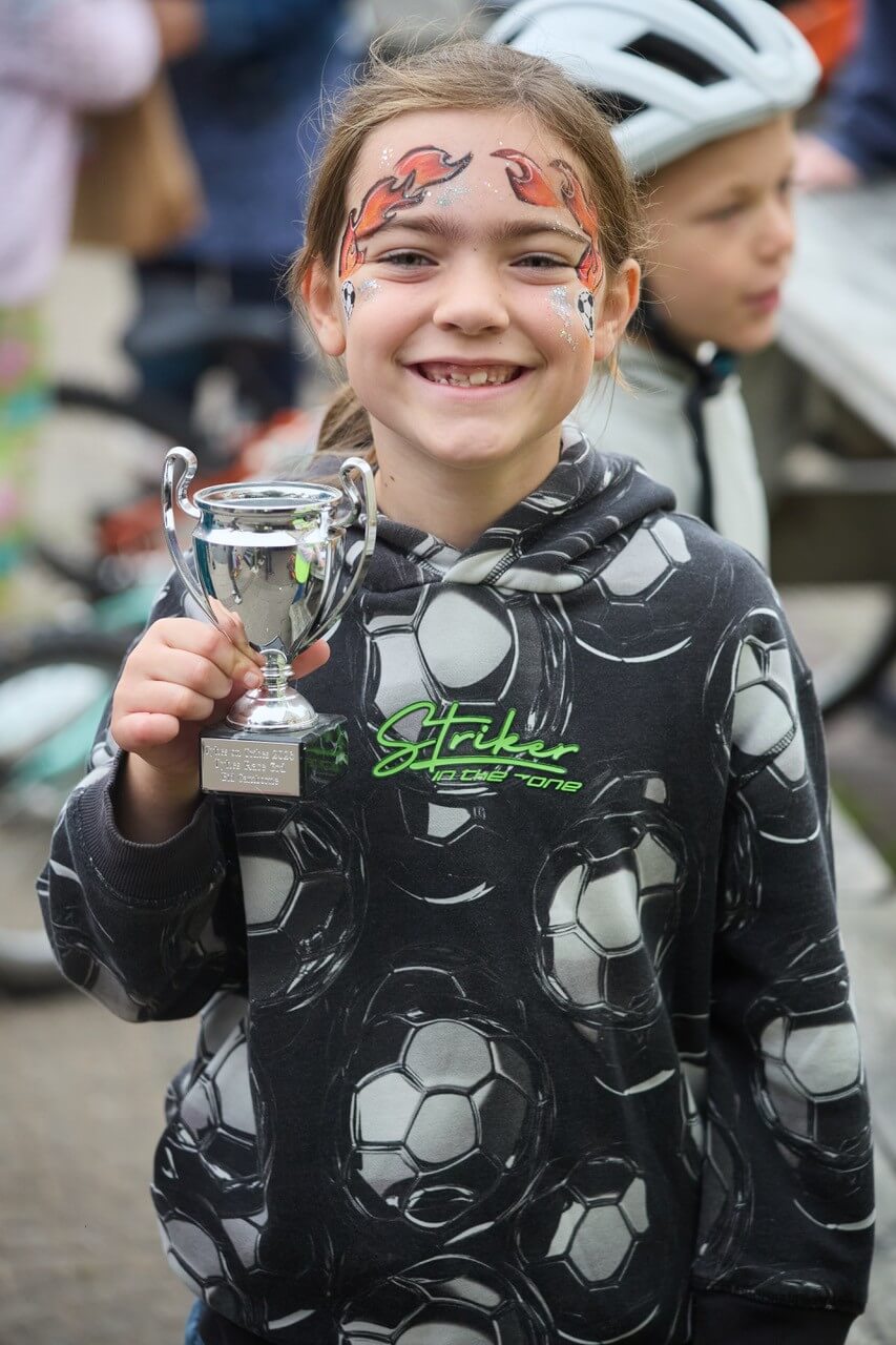 A girl with face paint holding her Tykes on Trikes trophy