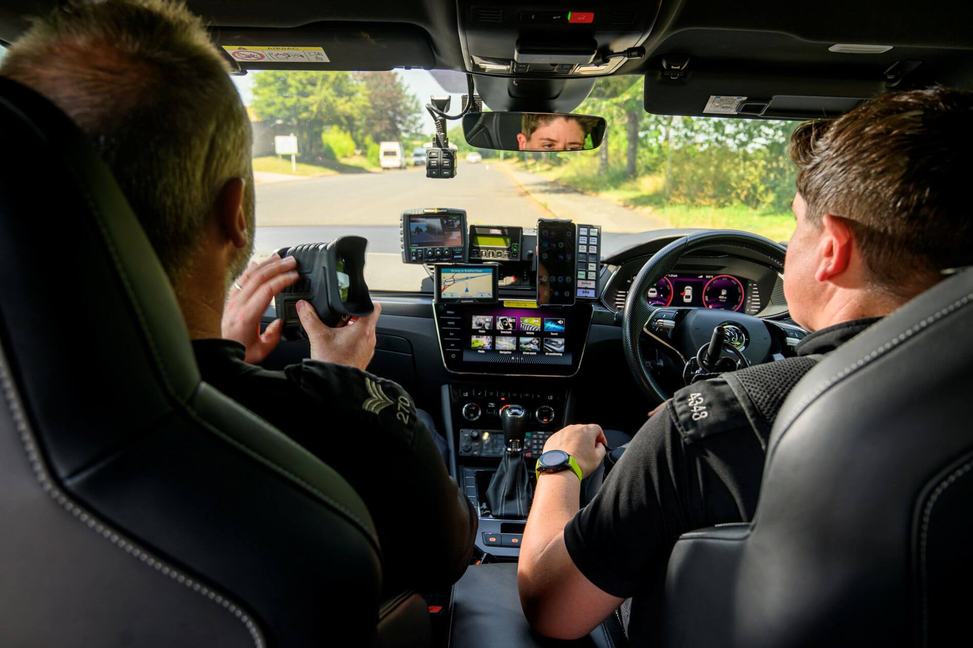 Police officers in a patrol car using a handheld number plate reader
