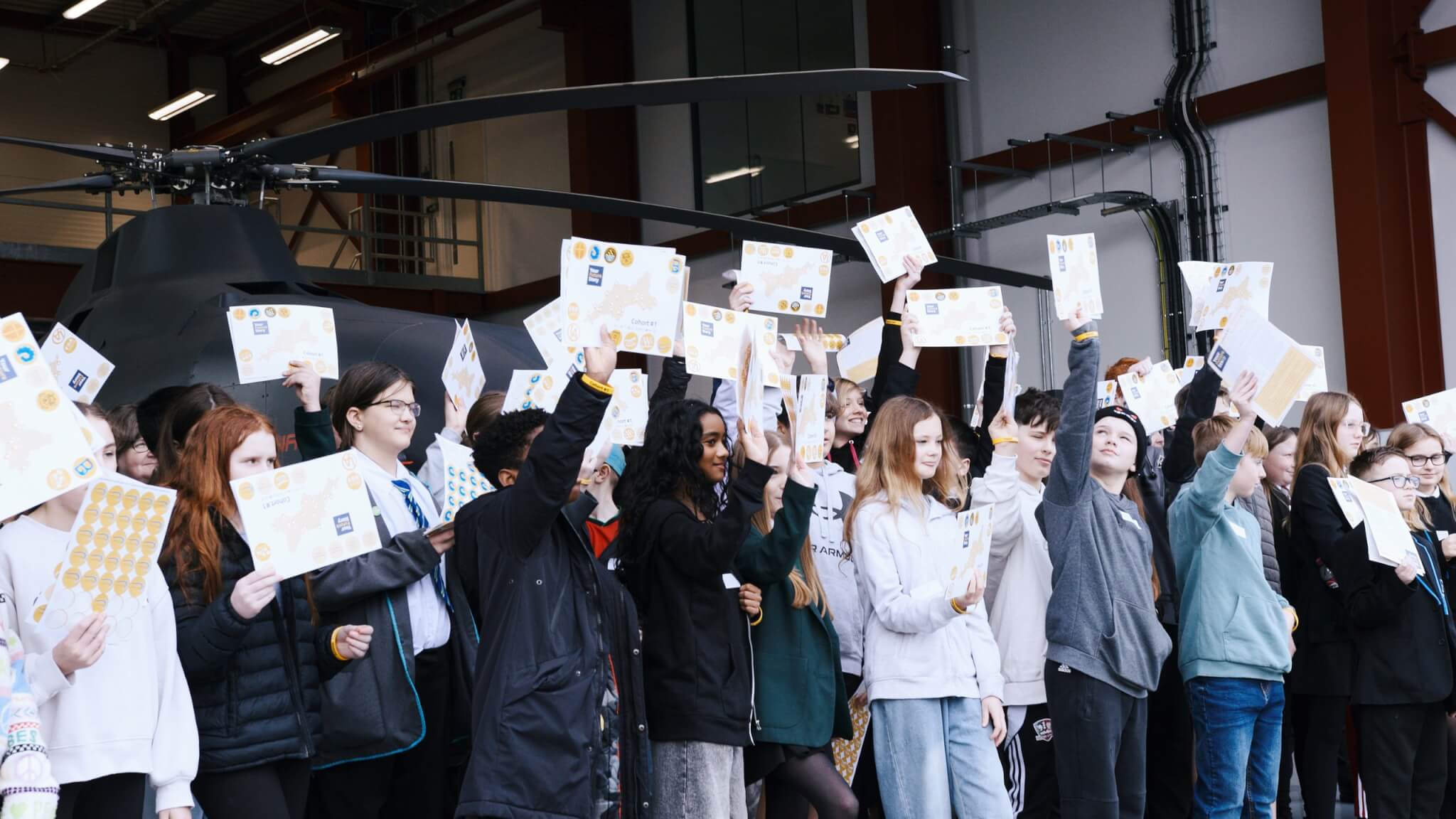 Students holding up Your Future Story Cohort #1 sheets in a hangar beside a helicopter