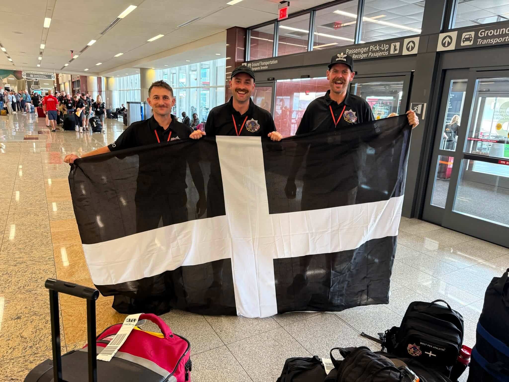 Three Cornwall firefighters holding a Cornish flag at Atlanta airport