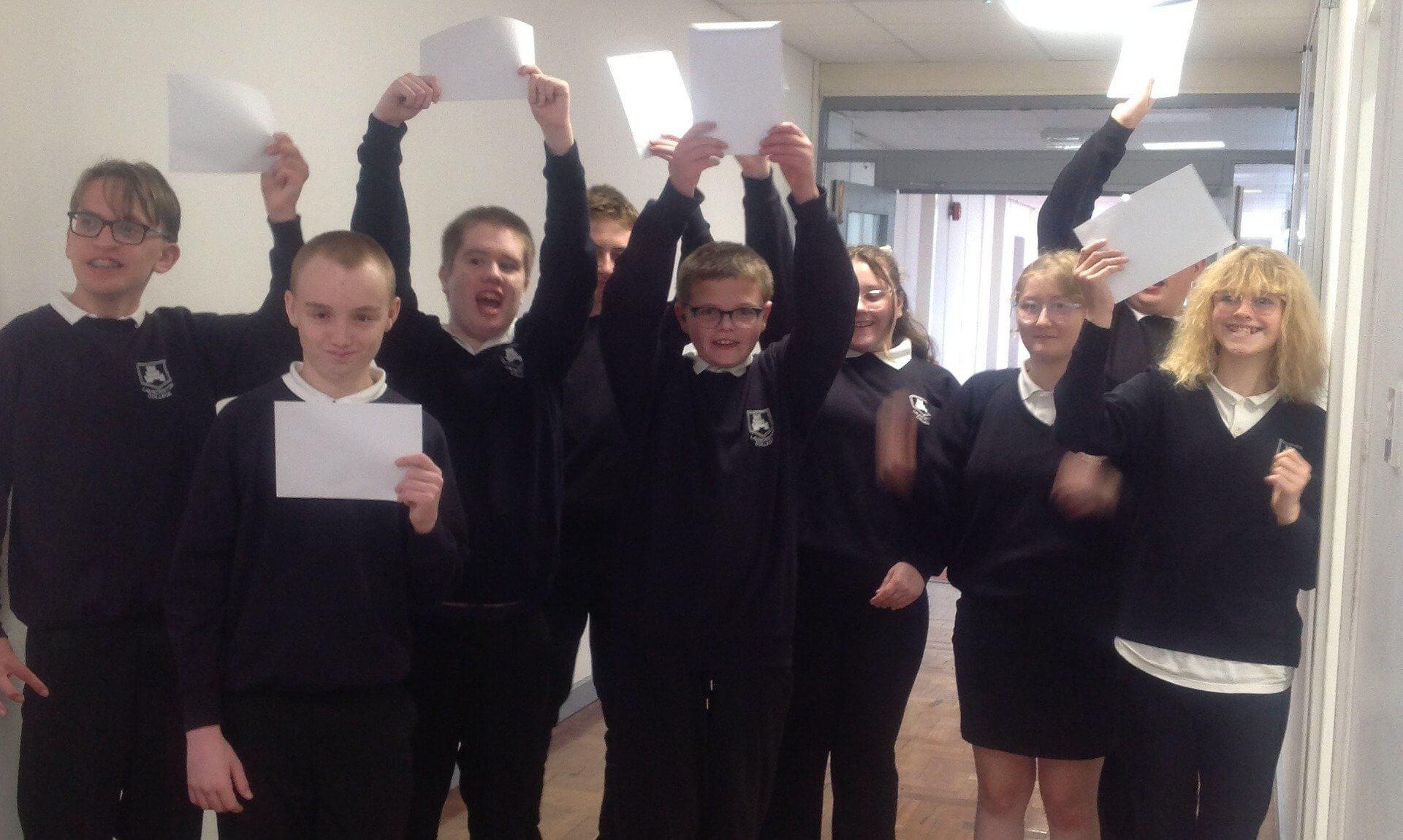 Launceston College ARB students in school uniform holding up their results in a corridor