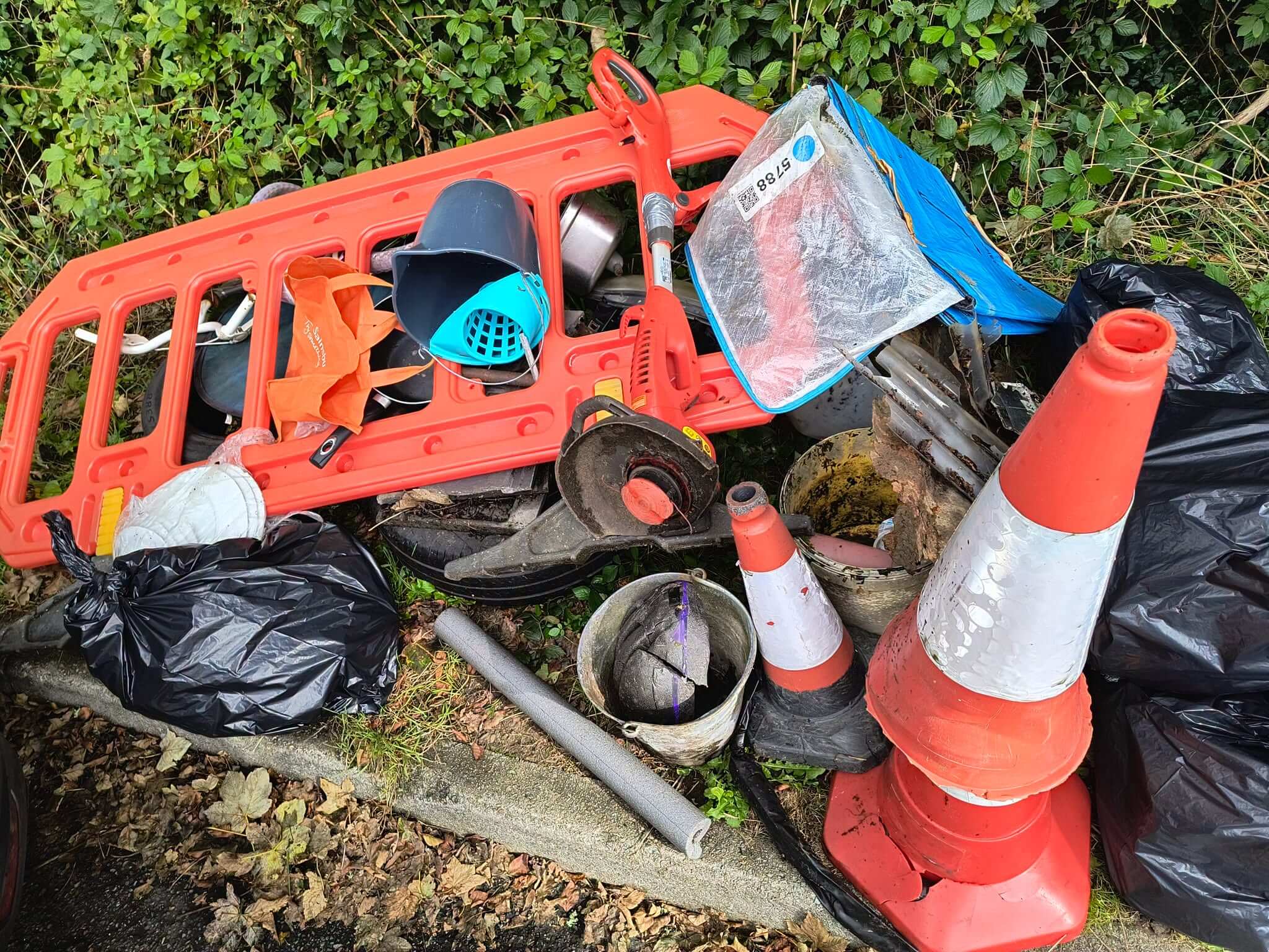 Pile of fly-tipped items including traffic cones, a strimmer and orange barrier in Bodmin