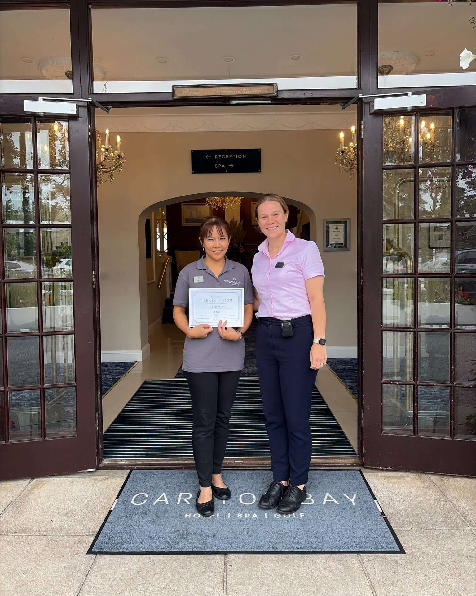 Tia and a colleague at the Carlyon Bay Hotel entrance with a ten years certificate of appreciation