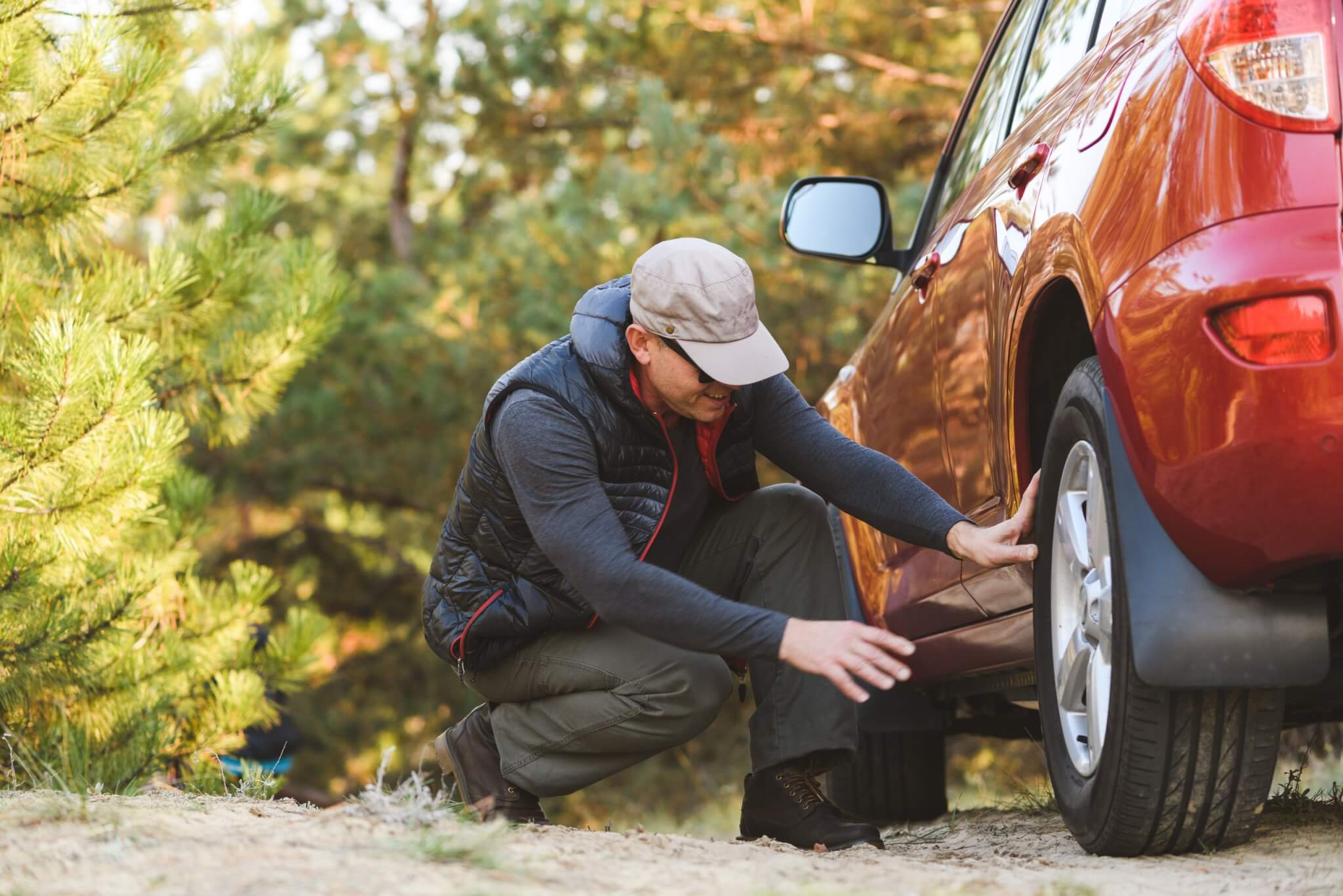 Driver crouching beside a red car to check a rear tyre