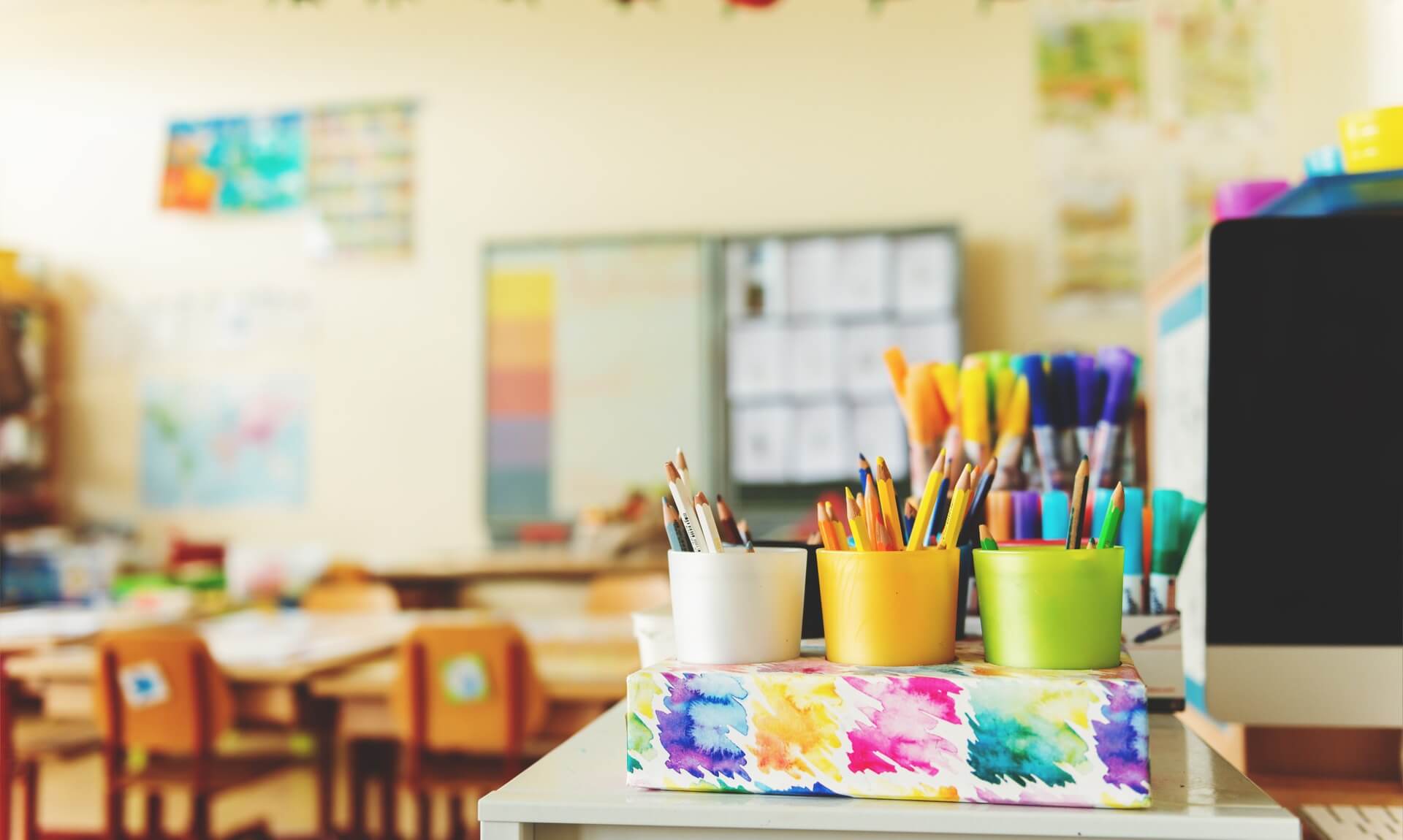 Colourful pots of pencils and pens on a school desk in a classroom