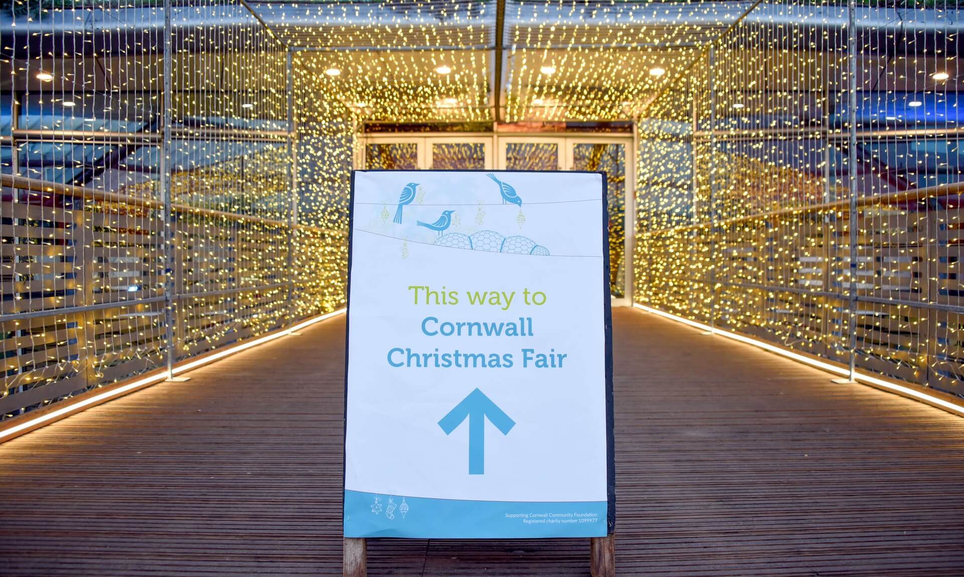 Sign reading This way to Cornwall Christmas Fair at the Eden Project, lit by fairy lights