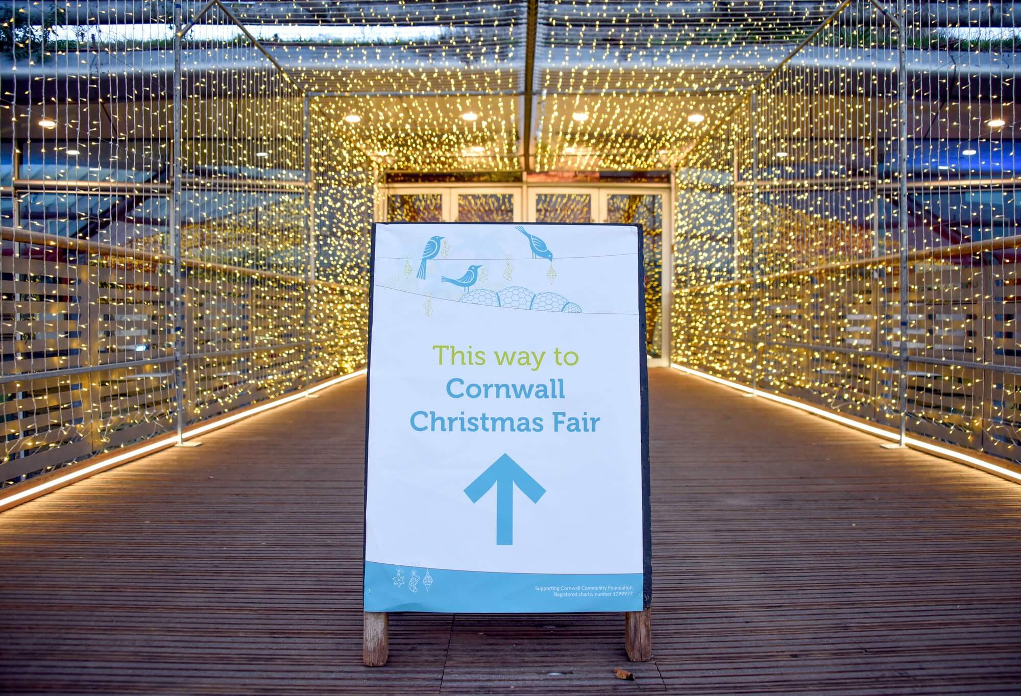 Sign reading This way to Cornwall Christmas Fair at the Eden Project, lit by fairy lights