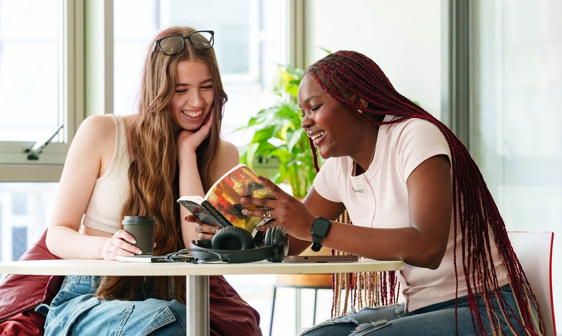 Two Cornwall College students laughing together over a book