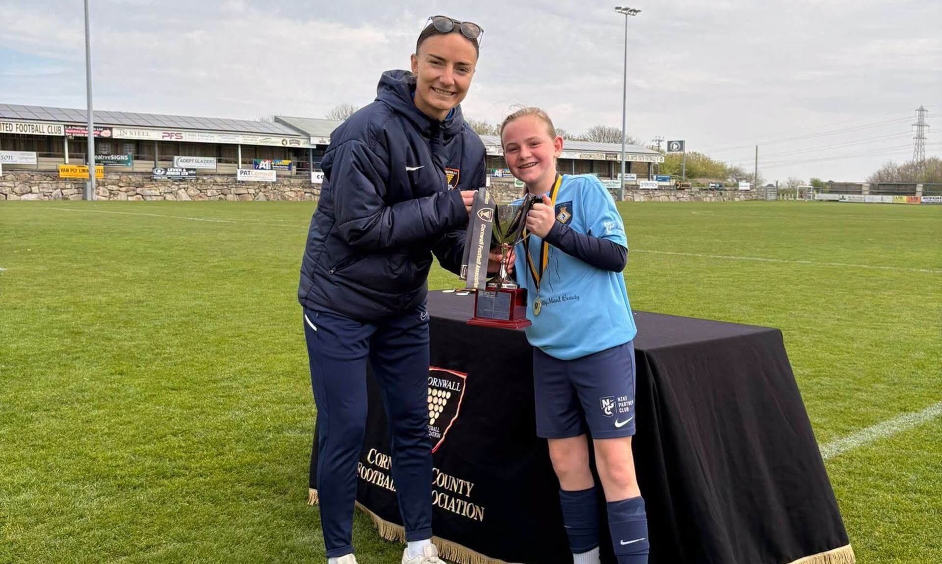 A coach presenting a trophy to a young player on a Cornwall football pitch