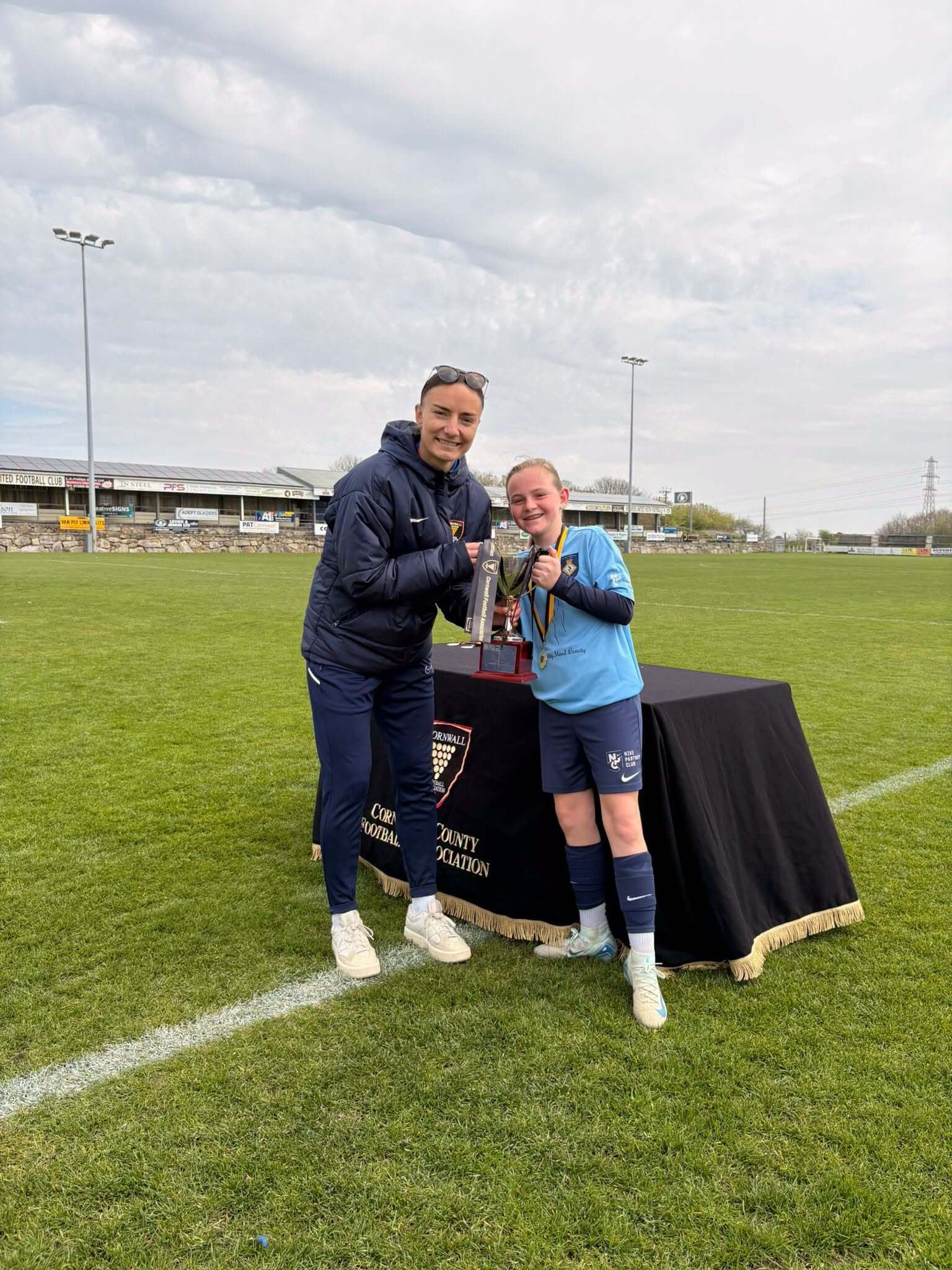 A coach presenting a trophy to a young player on a Cornwall football pitch