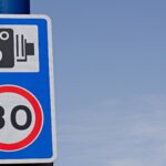 A speed camera warning sign with a 30mph limit roundel against a blue sky