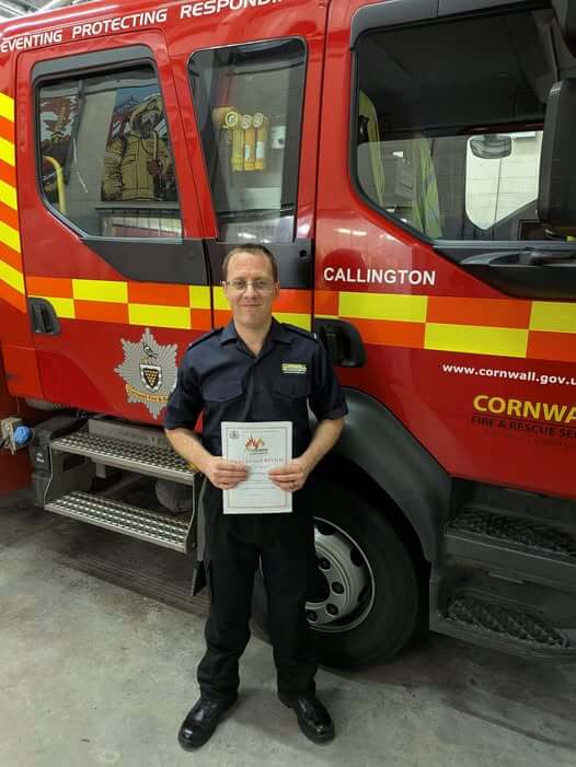 Dan Chowings holding his qualification certificate in front of a Callington fire engine
