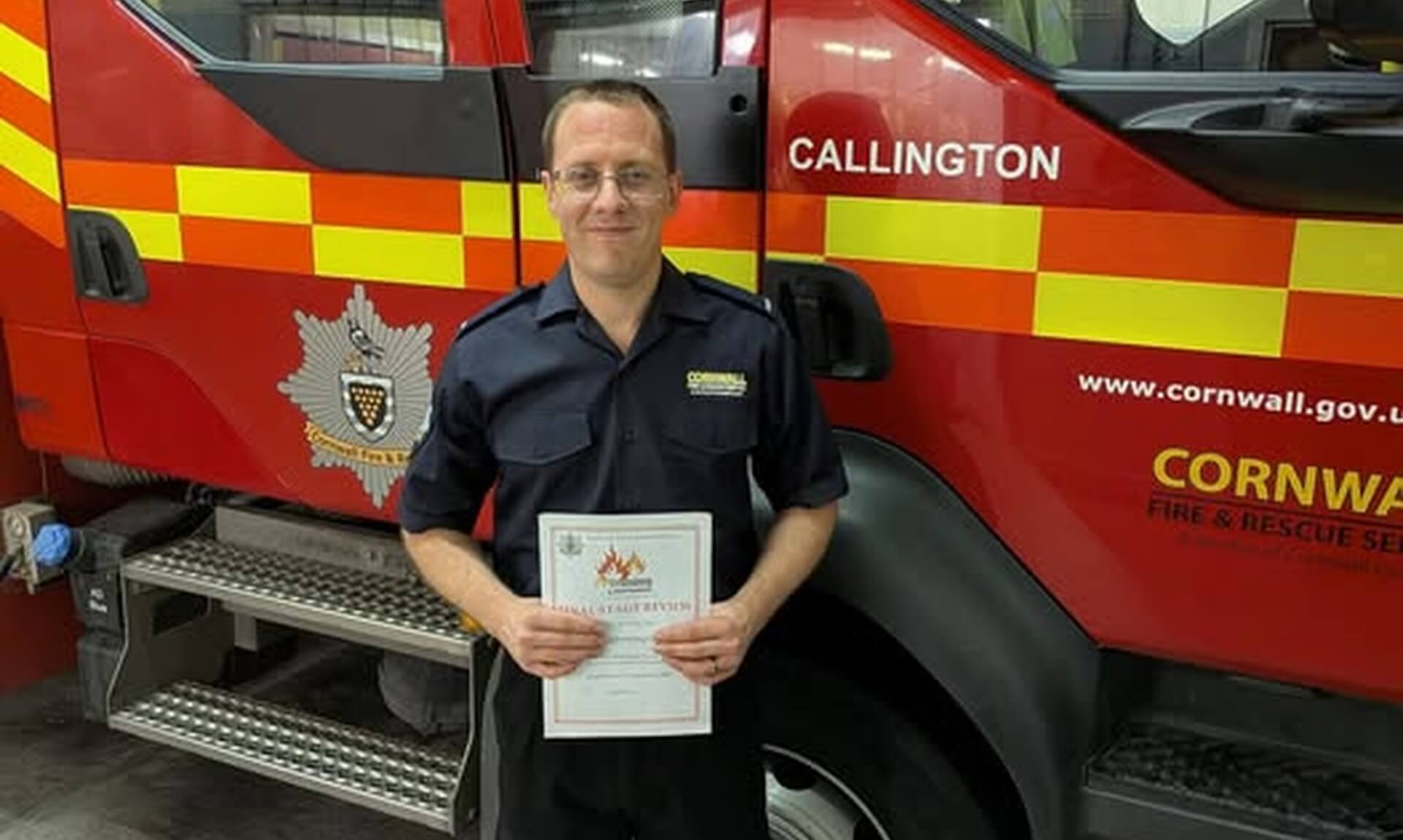Dan Chowings holding his qualification certificate in front of a Callington fire engine