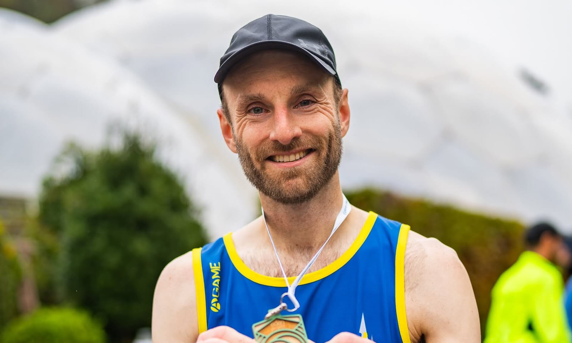 A runner holding a finisher's medal in front of the Eden Project biomes