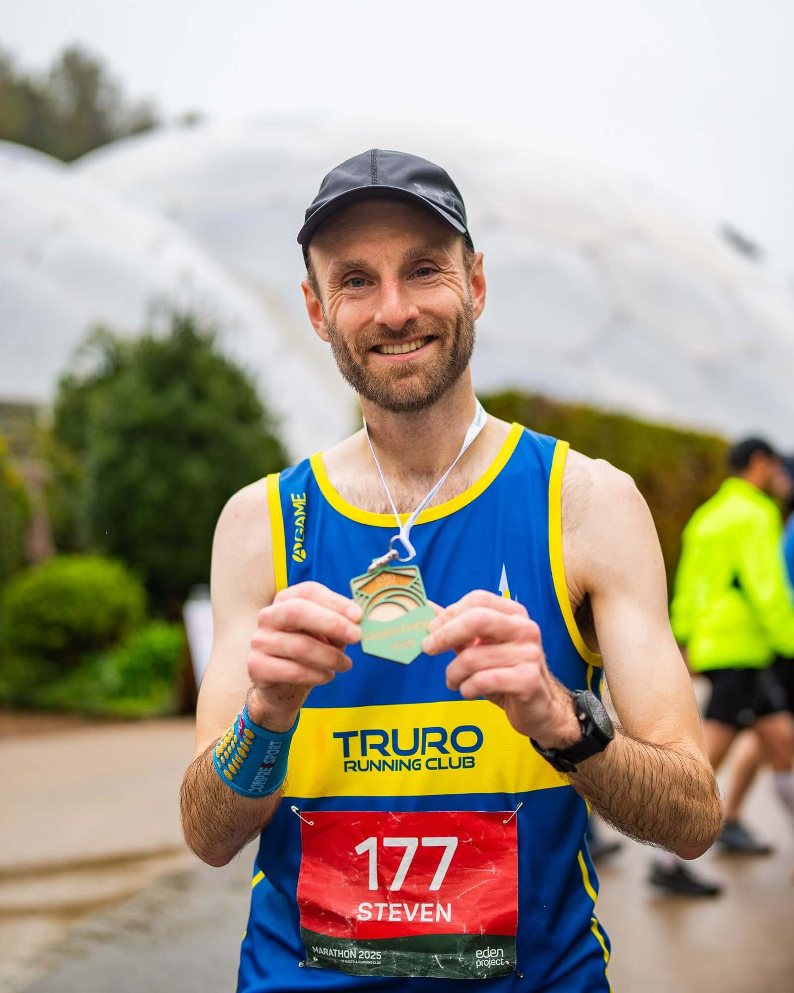 A runner holding a finisher's medal in front of the Eden Project biomes