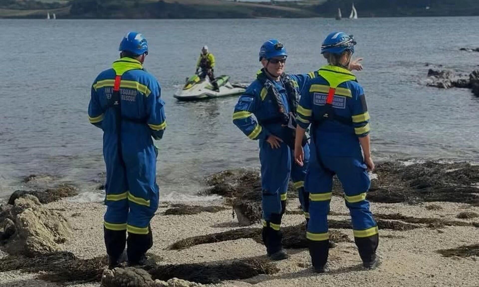 Falmouth Coastguard Rescue Team officers on a beach with a coastguard personal watercraft offshore