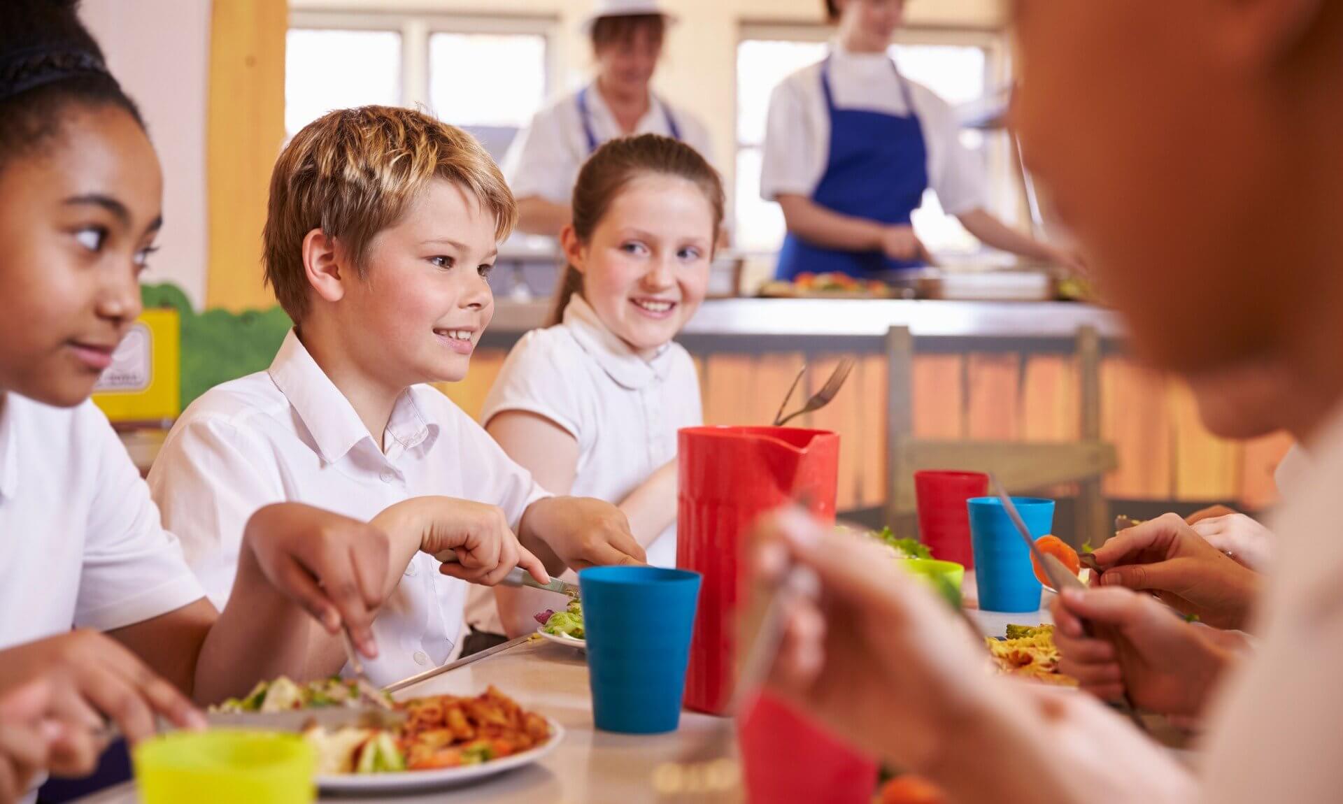 Primary school children eating lunch together in a school canteen