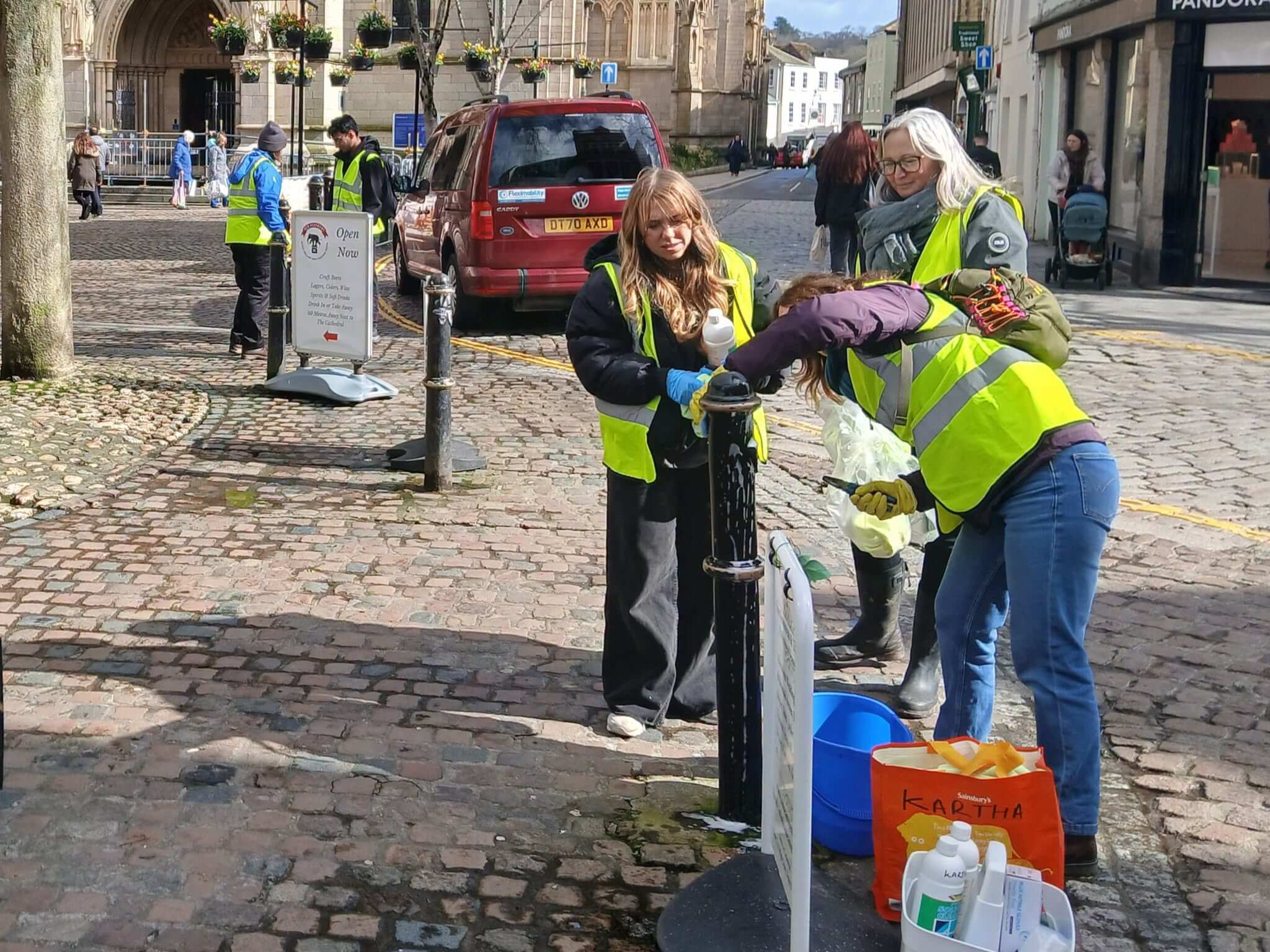 Volunteers in hi-vis vests cleaning a lamp post in Truro city centre