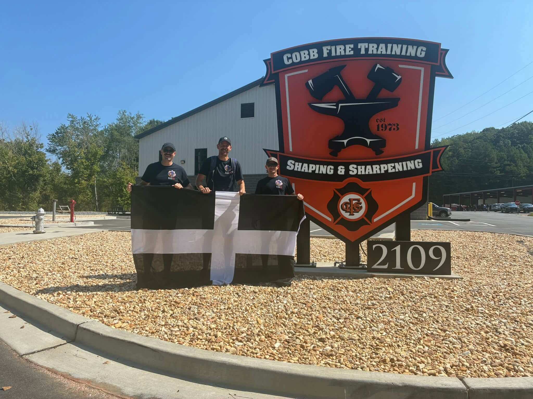 Three Cornwall firefighters holding a Cornish flag in front of the Cobb Fire Training sign in Atlanta