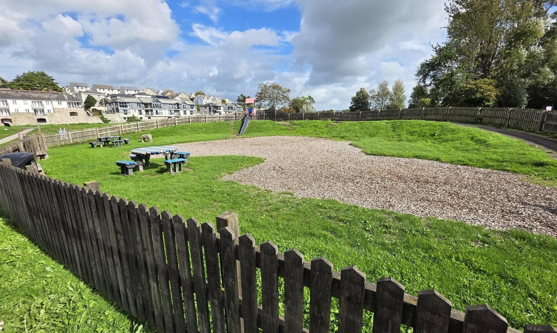 Jubilee Play Area in Wadebridge with bark chip, picnic tables and a slide behind a wooden fence