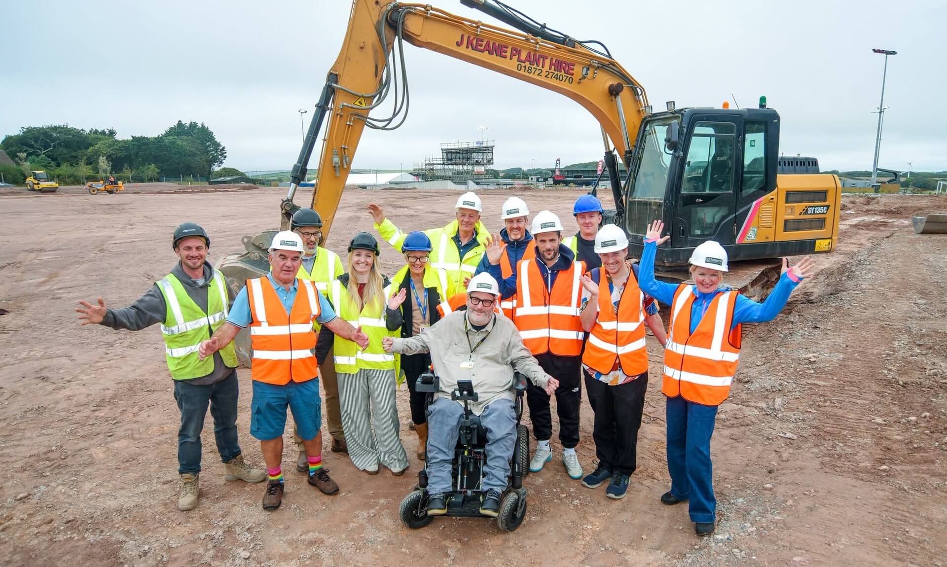 Group in hard hats and hi-vis in front of a digger at the Truro Sports Hub 3G pitch site, Langarth