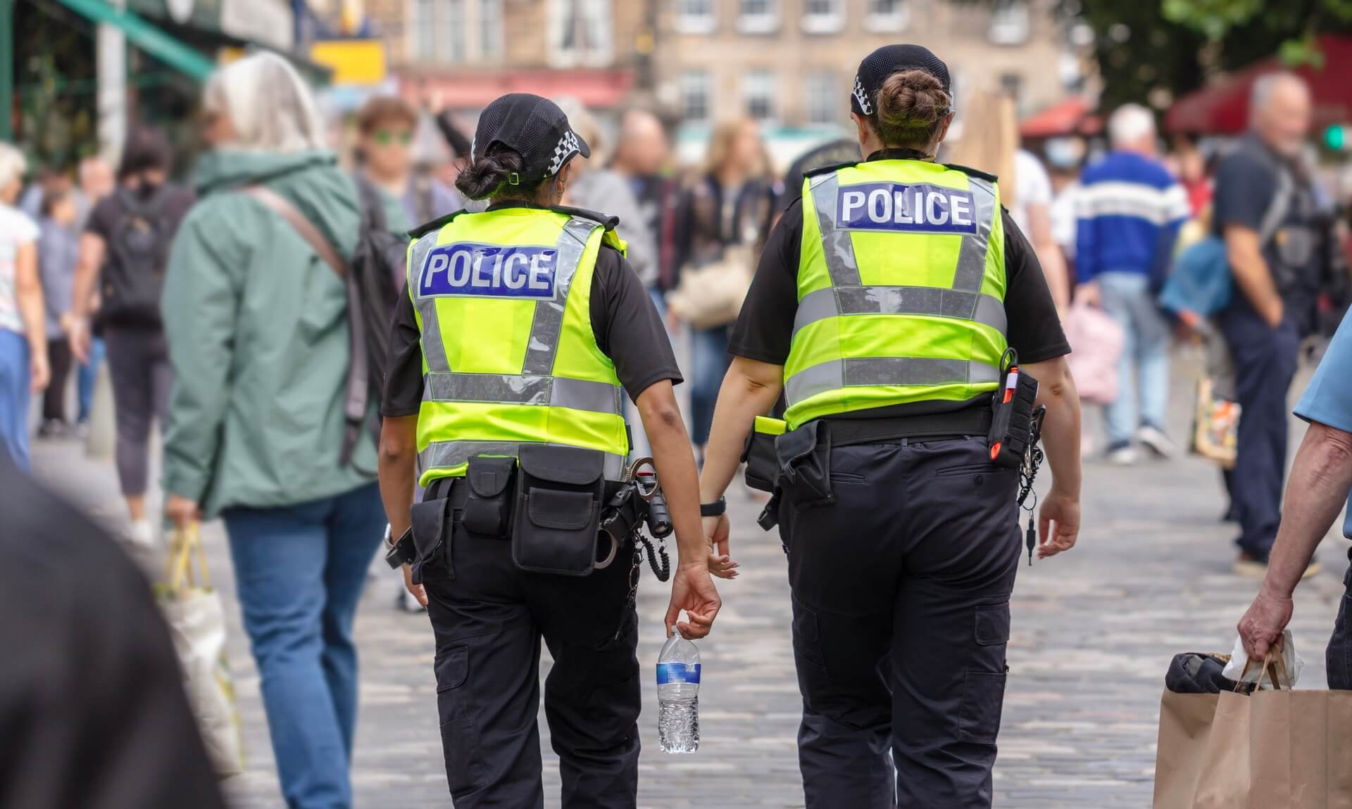 Two police officers walking through a busy UK high street from behind
