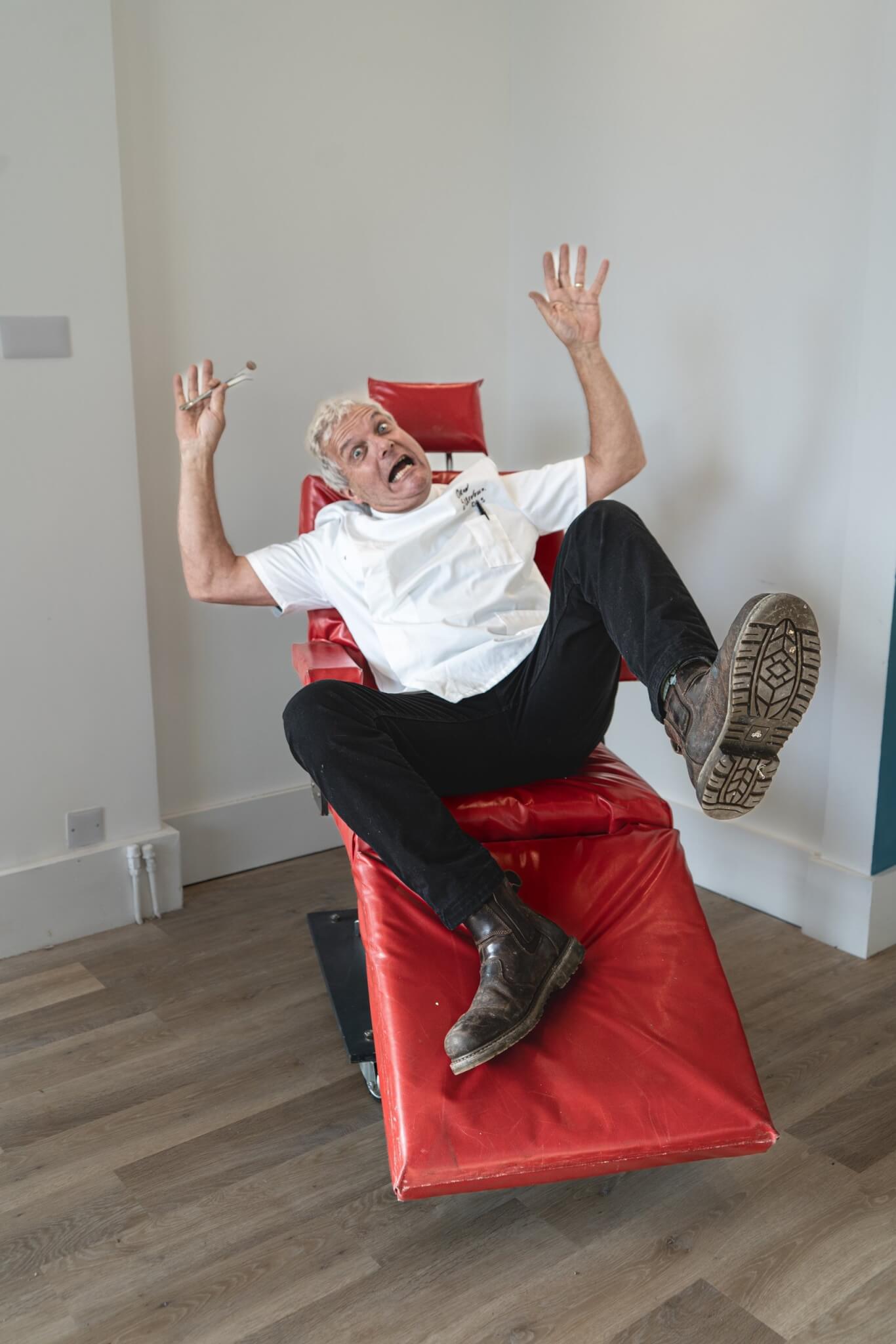 A cast member in a dentist's coat tumbles back in a red dentist's chair
