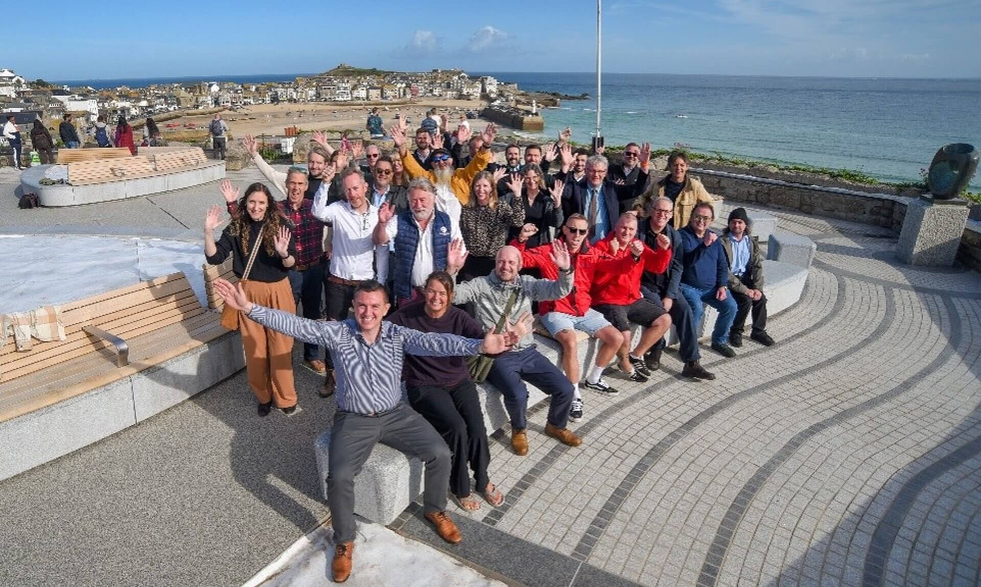 Project partners wave from the new granite seating on the Malakoff in St Ives with the harbour behind