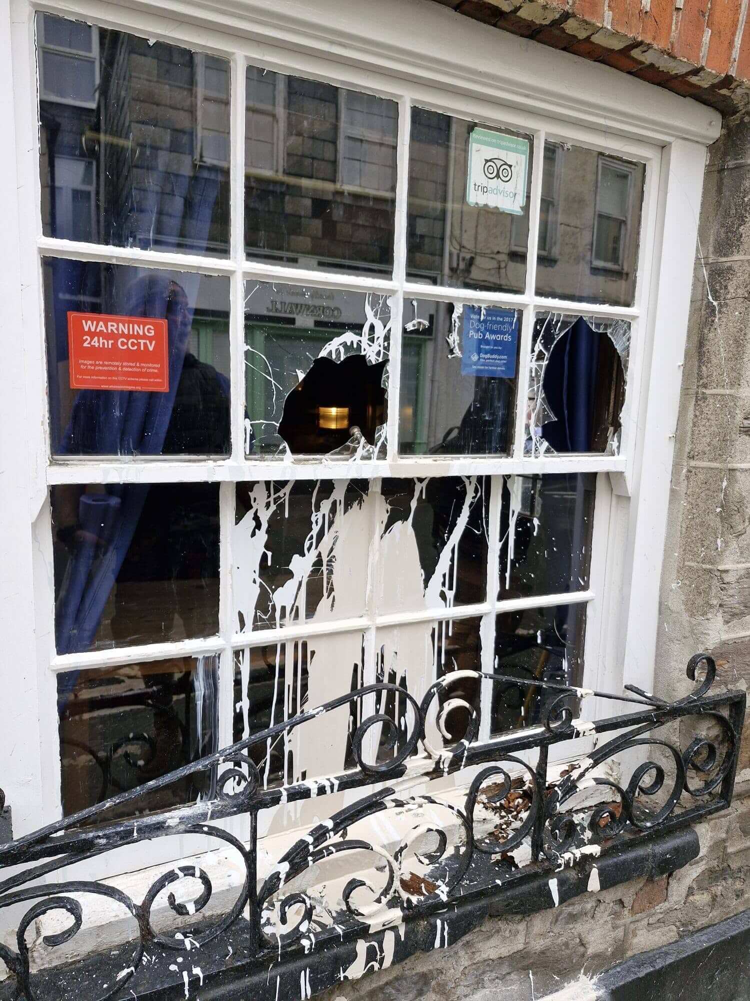 A smashed sash window pane splattered with white paint in Mevagissey