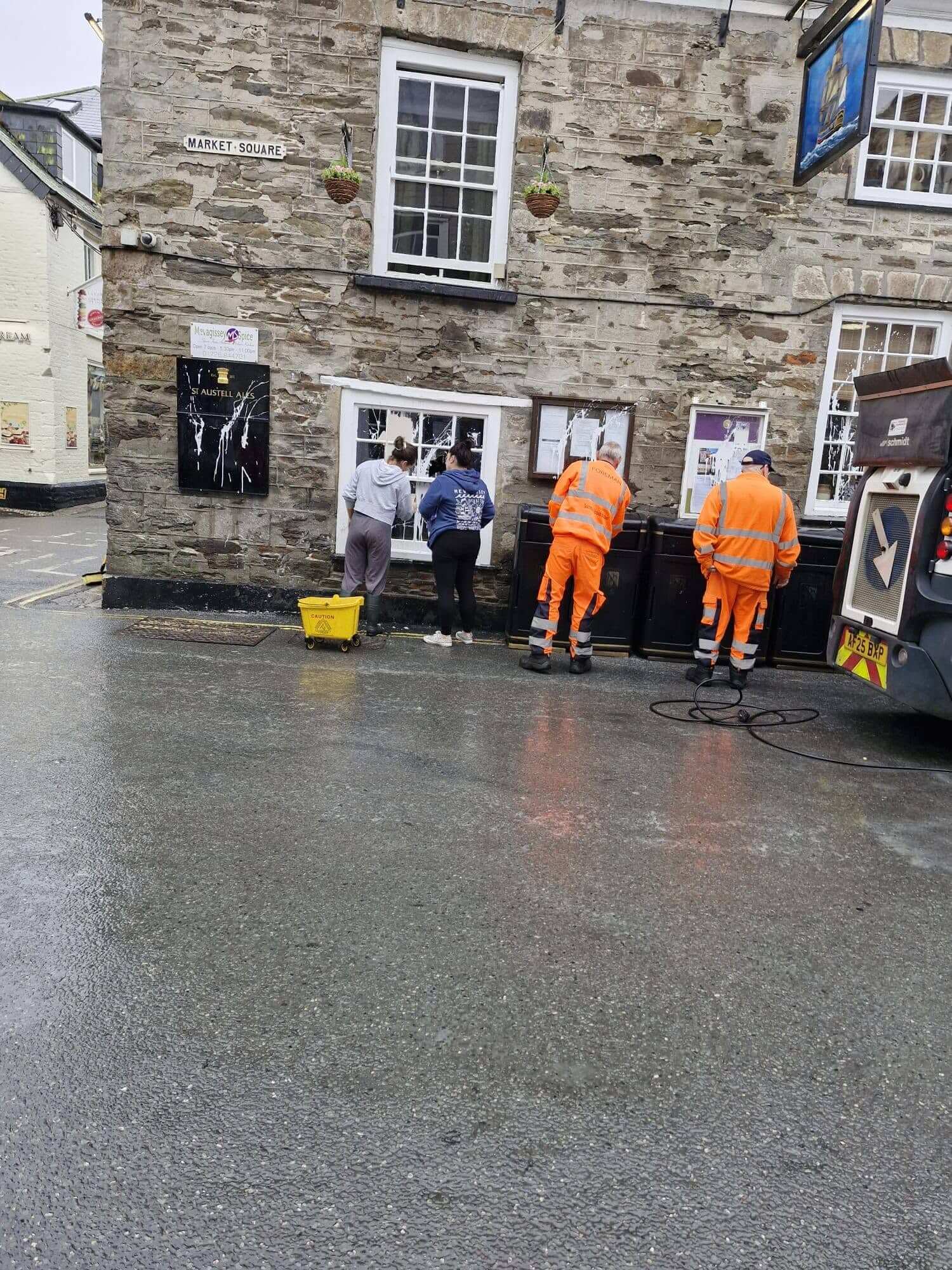 Residents and council contractors cleaning paint from shopfronts in Mevagissey's Market Square