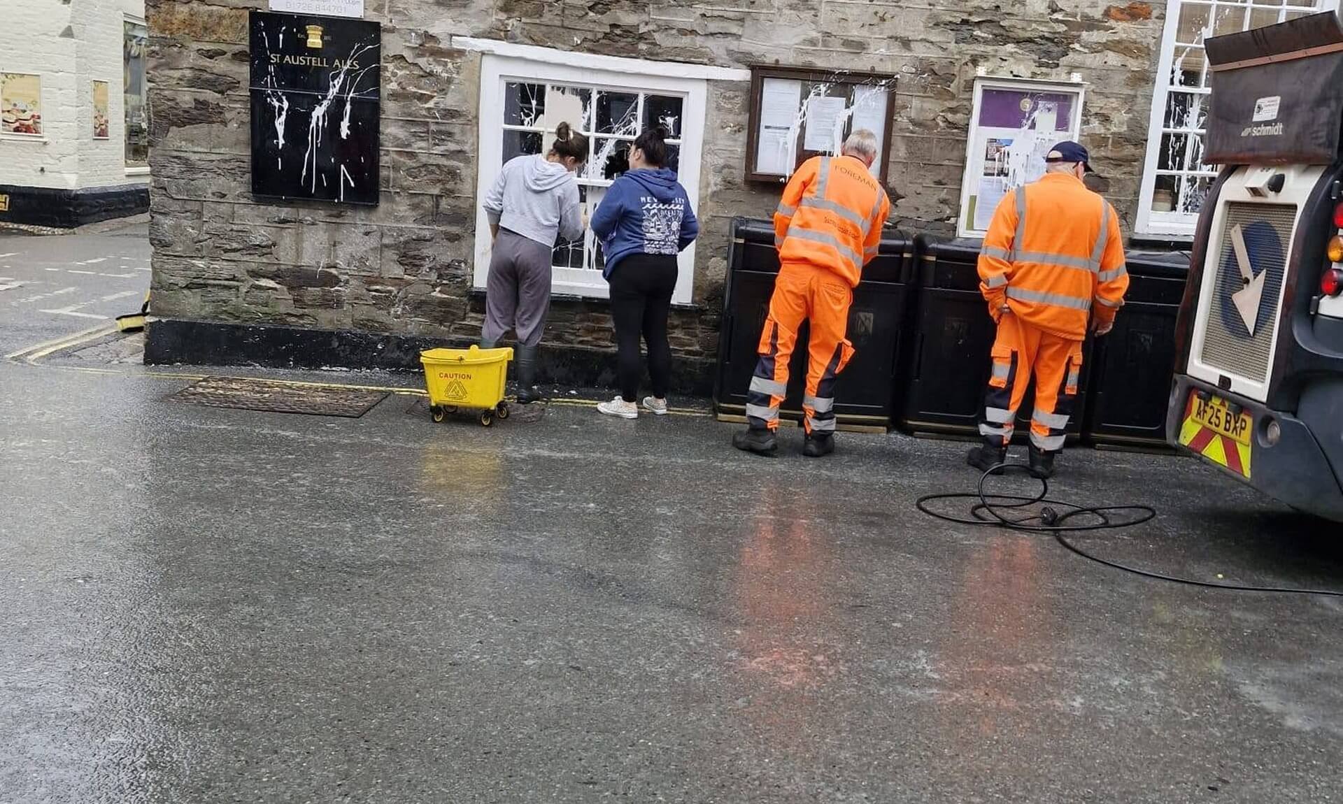 Residents and council contractors cleaning paint from shopfronts in Mevagissey's Market Square