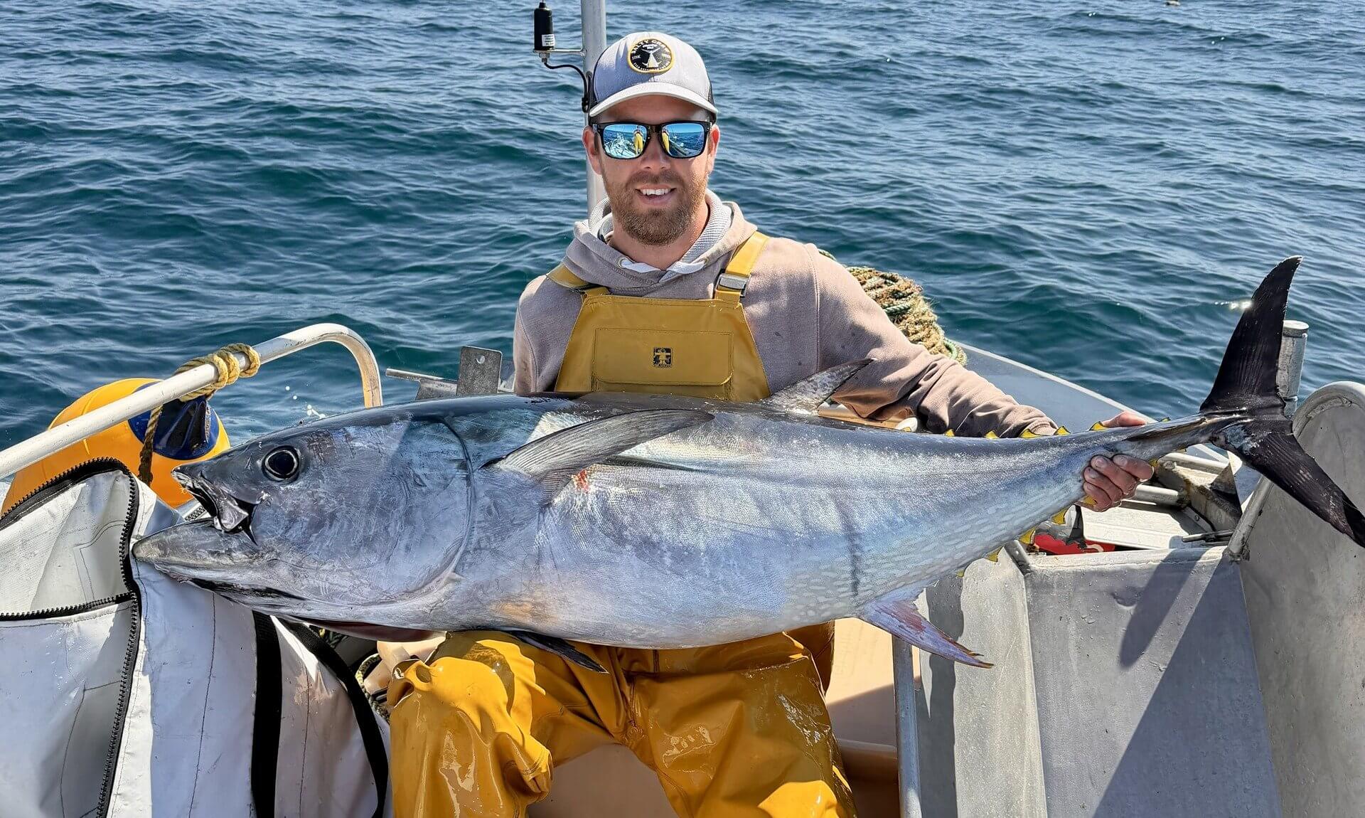Fisherman holding a bluefin tuna aboard a small boat at sea