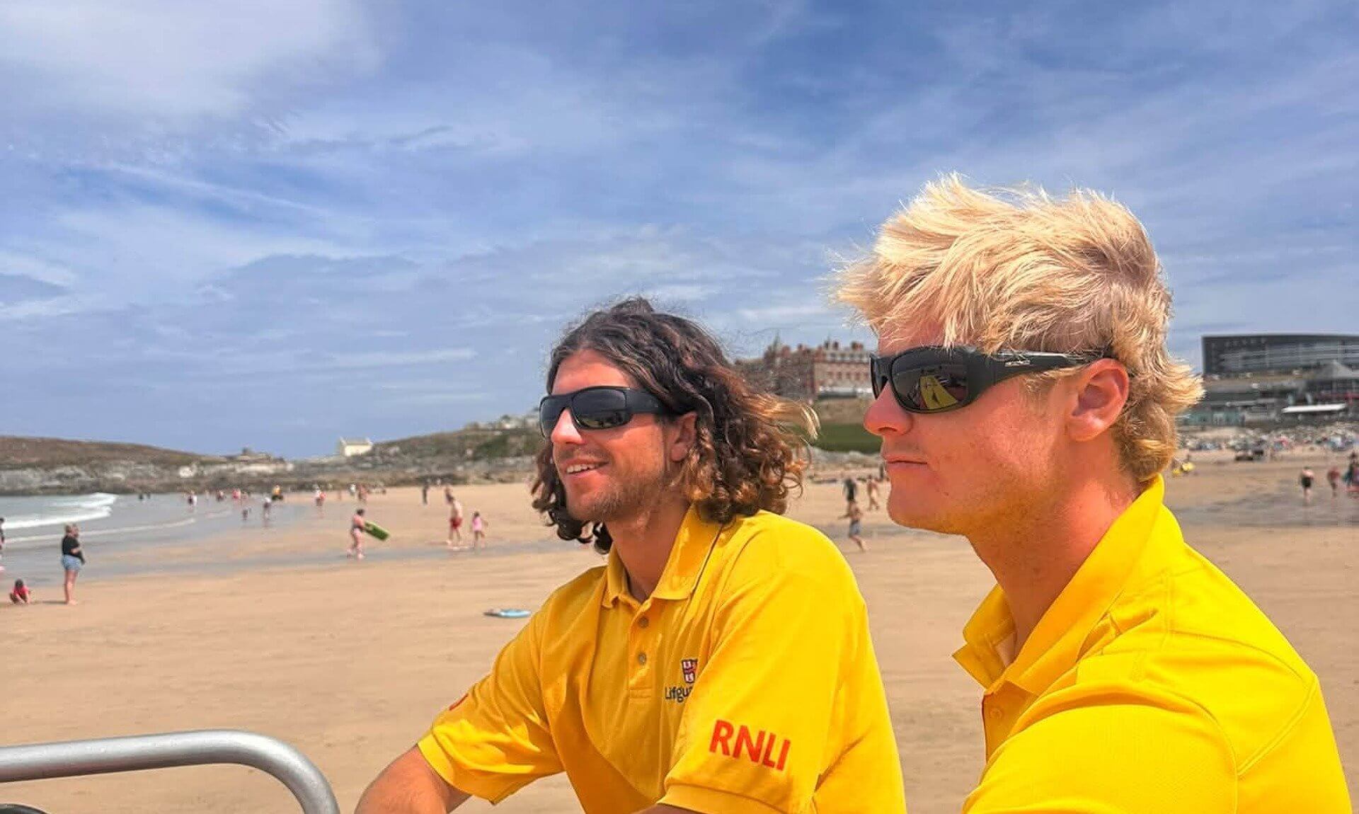 Two RNLI lifeguards in yellow tops watching a busy Newquay beach