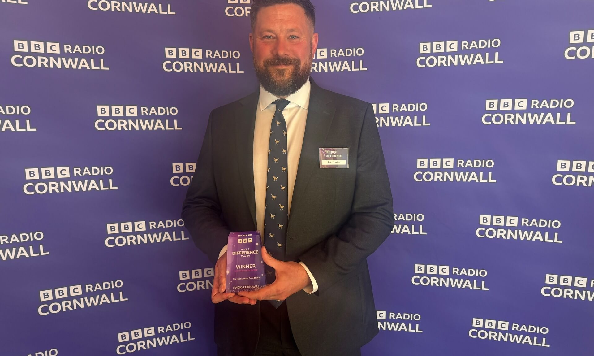 Ben Jordan holding his BBC Make a Difference Award in front of a BBC Radio Cornwall backdrop