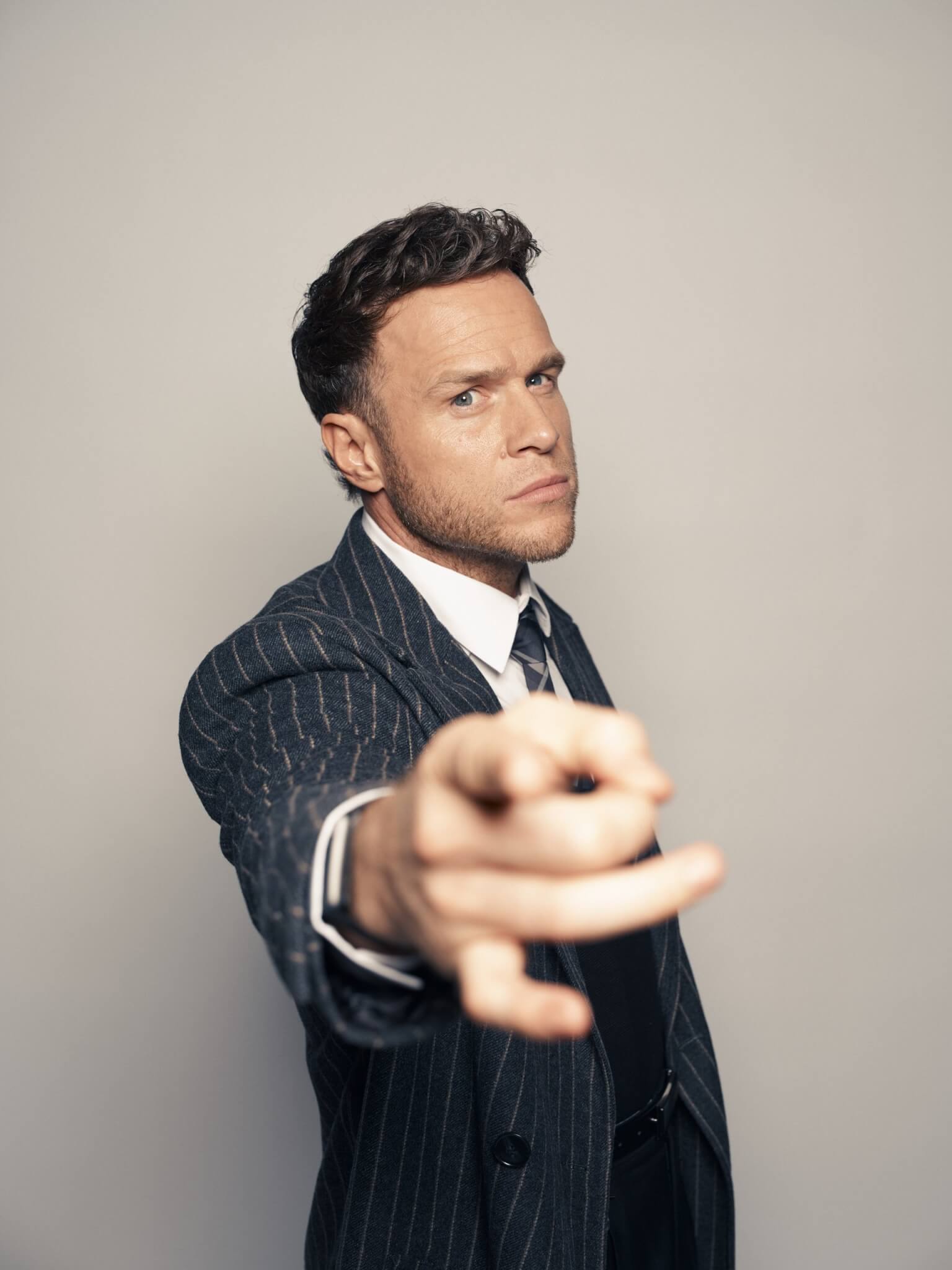 Olly Murs in a pinstripe suit pointing towards the camera