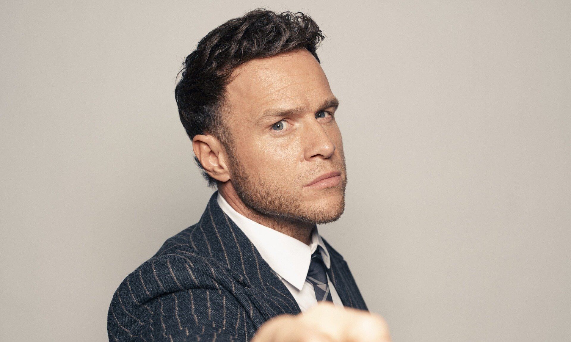 Olly Murs in a pinstripe suit pointing towards the camera