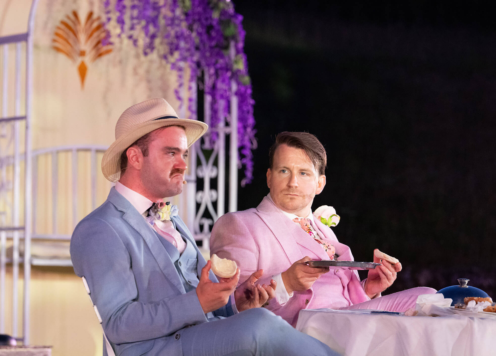 Two male cast members in 1920s suits seated at the Minack Theatre in the evening