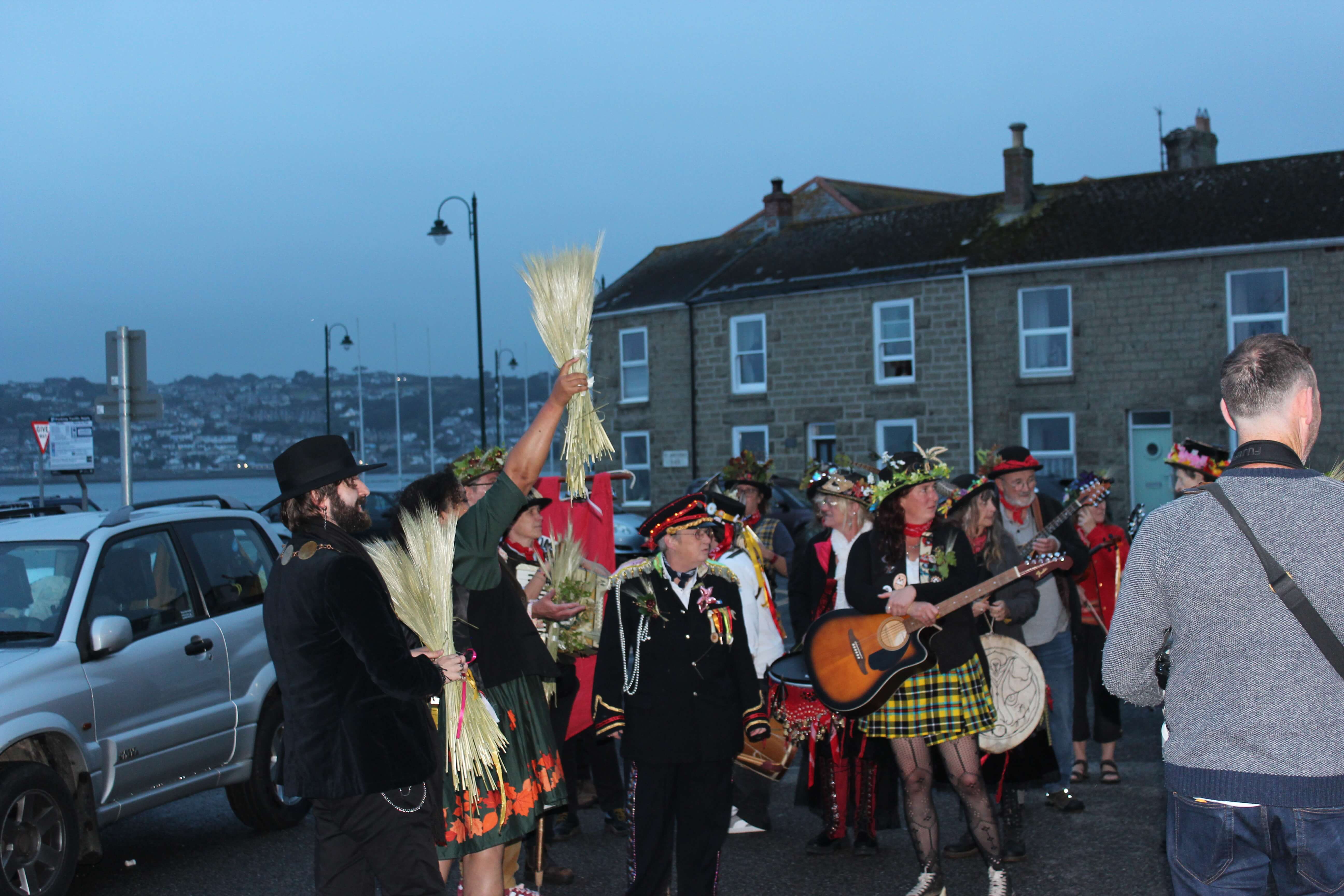 Guldize procession in Penzance, a bundle of corn held aloft by the harbour at dusk