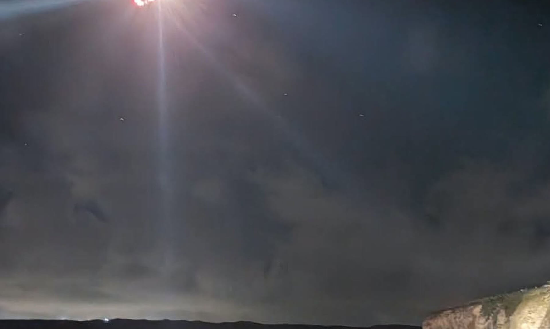 A rescuer's headtorch beam cuts through the night sky above the cliffs and sea at Perranporth