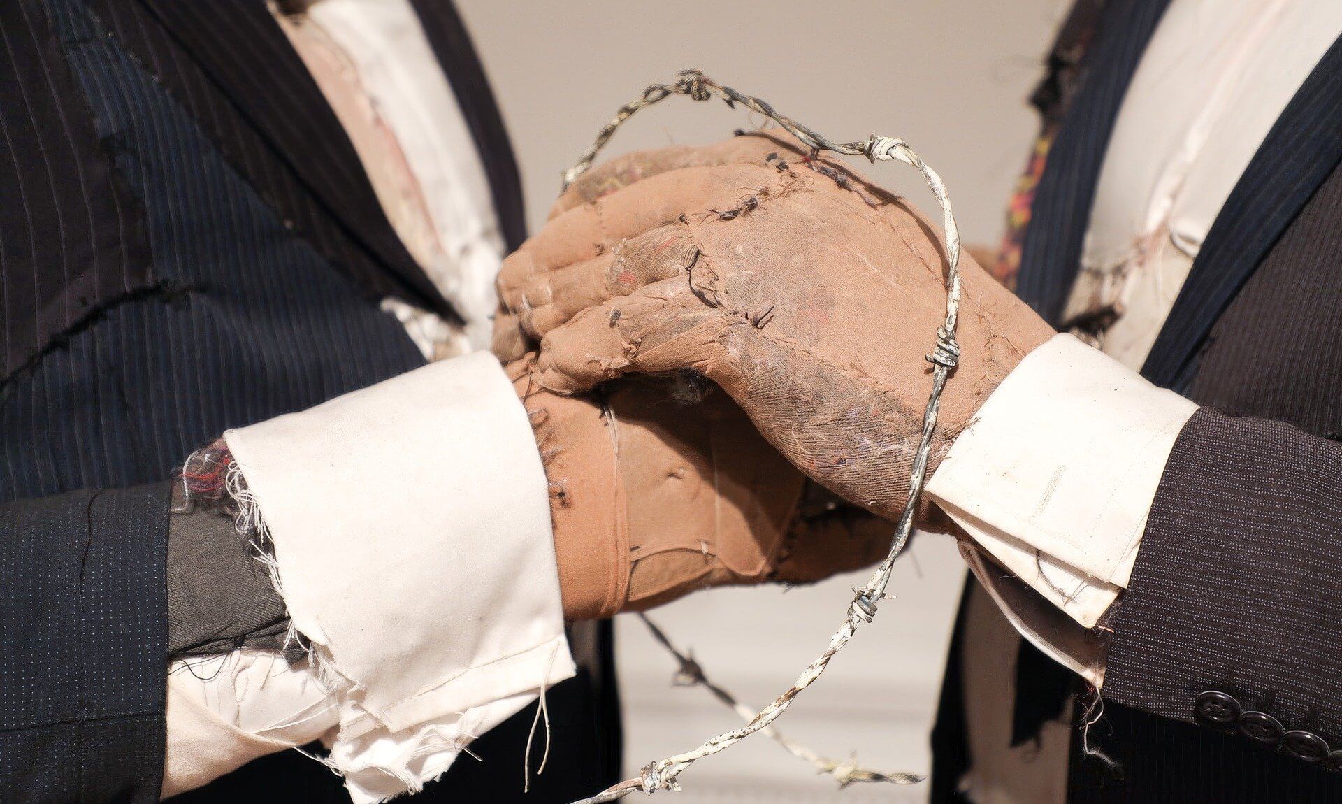 Sewn fabric hands clasped inside a loop of barbed wire in Tim Shaw's sculpture Pin It On Them