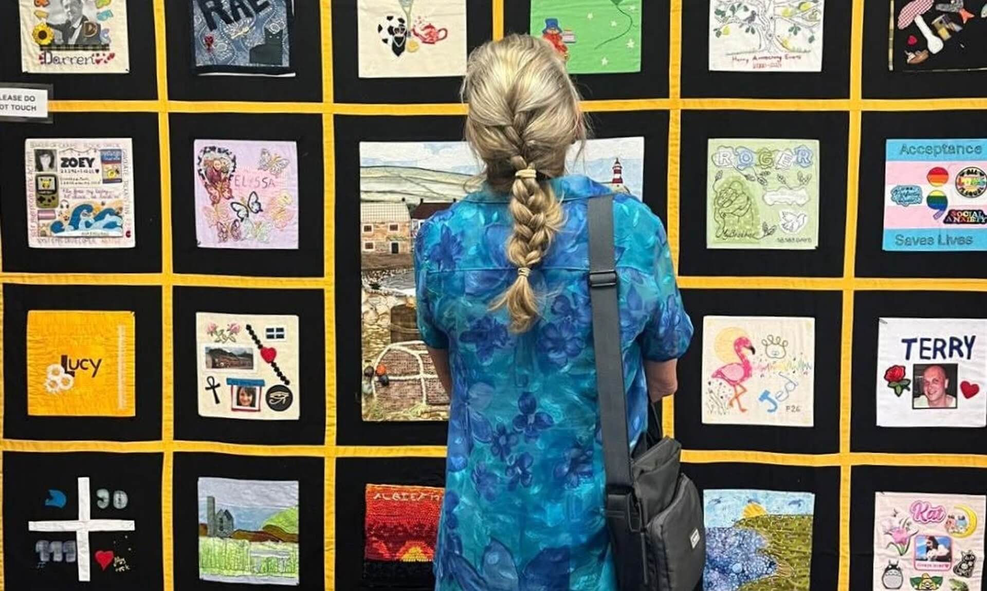 Visitor looking at a wall of Speak Their Name memorial quilt squares