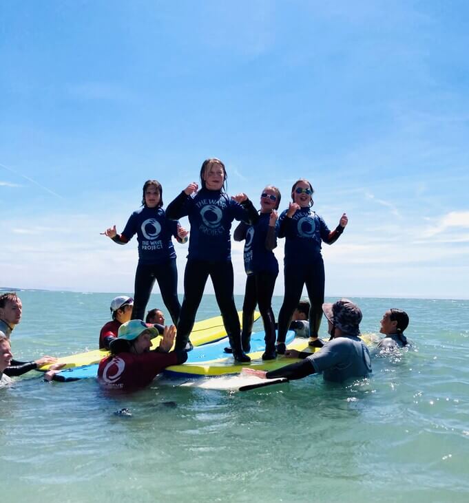 Young people in Wave Project rash vests standing on surfboards in the sea