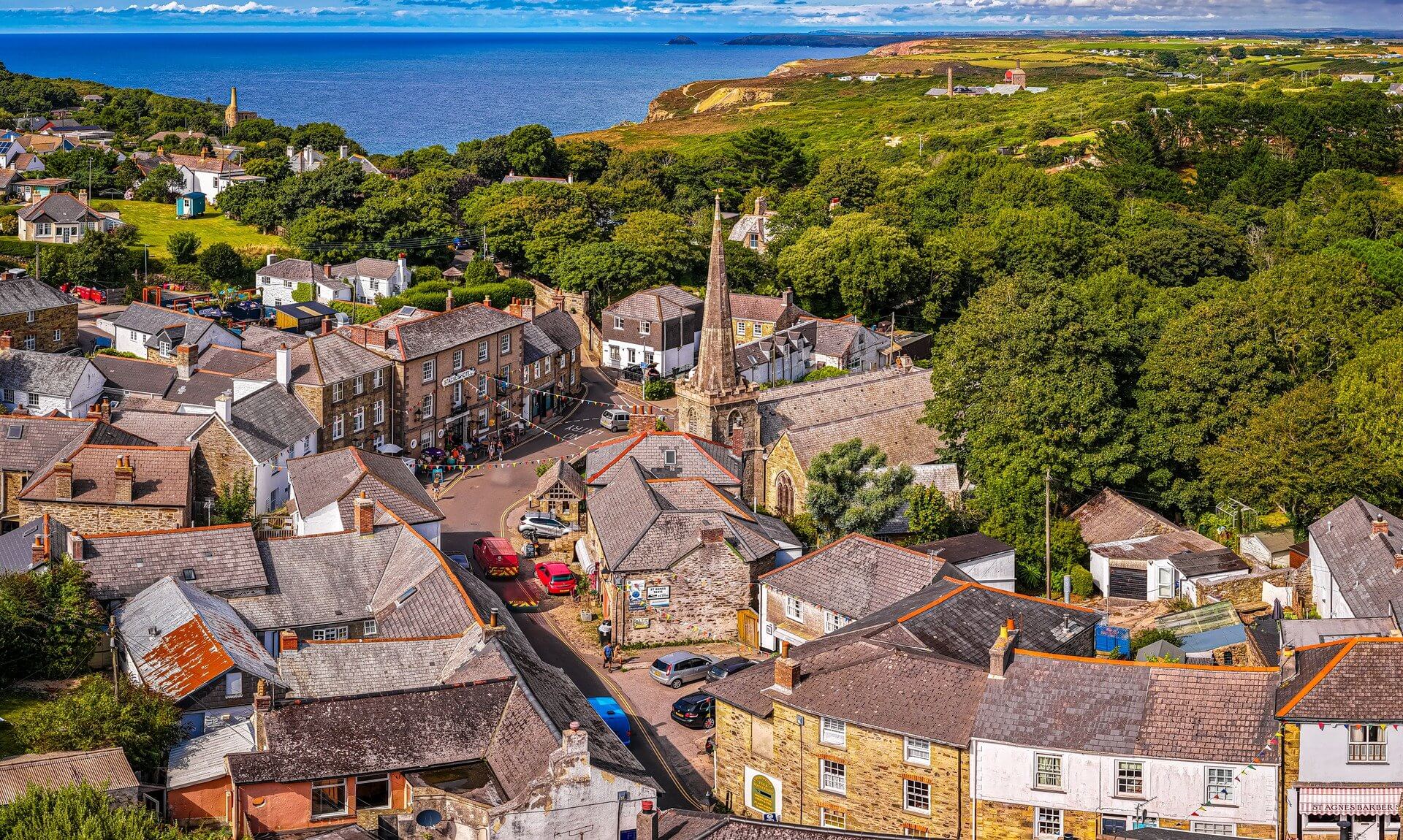 Aerial view of St Agnes village centre, with the church spire, rooftops and the north Cornwall coast beyond