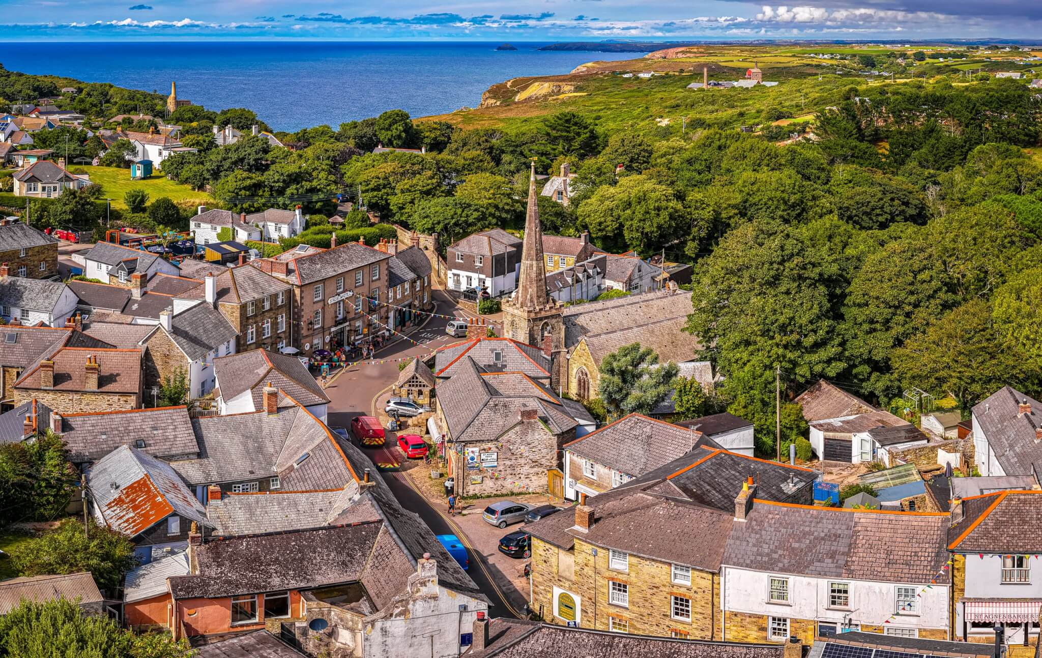 Aerial view of St Agnes village centre, with the church spire, rooftops and the north Cornwall coast beyond