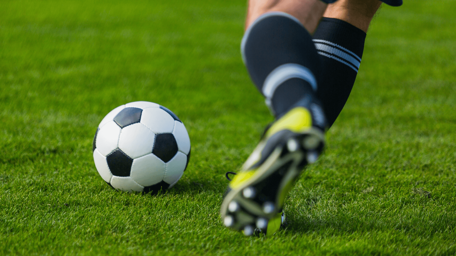 Footballer's boot about to strike the ball on a grass pitch